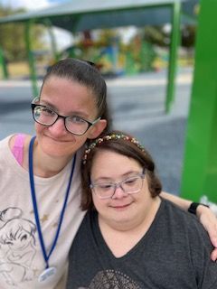 Two women are posing for a picture together in a park . one of the women is wearing glasses.