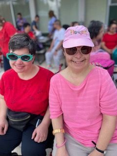 Two women wearing pink shirts and sunglasses are sitting next to each other.