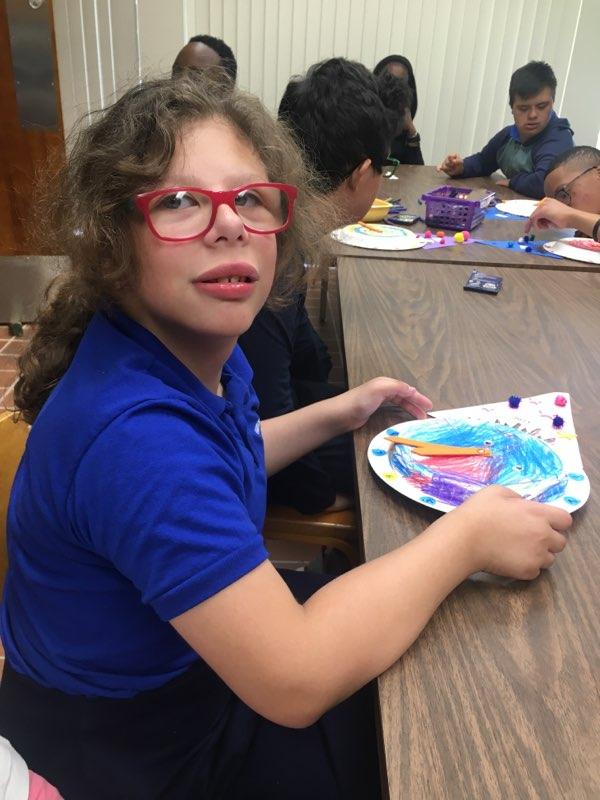 A girl wearing glasses sits at a table with a plate of paint