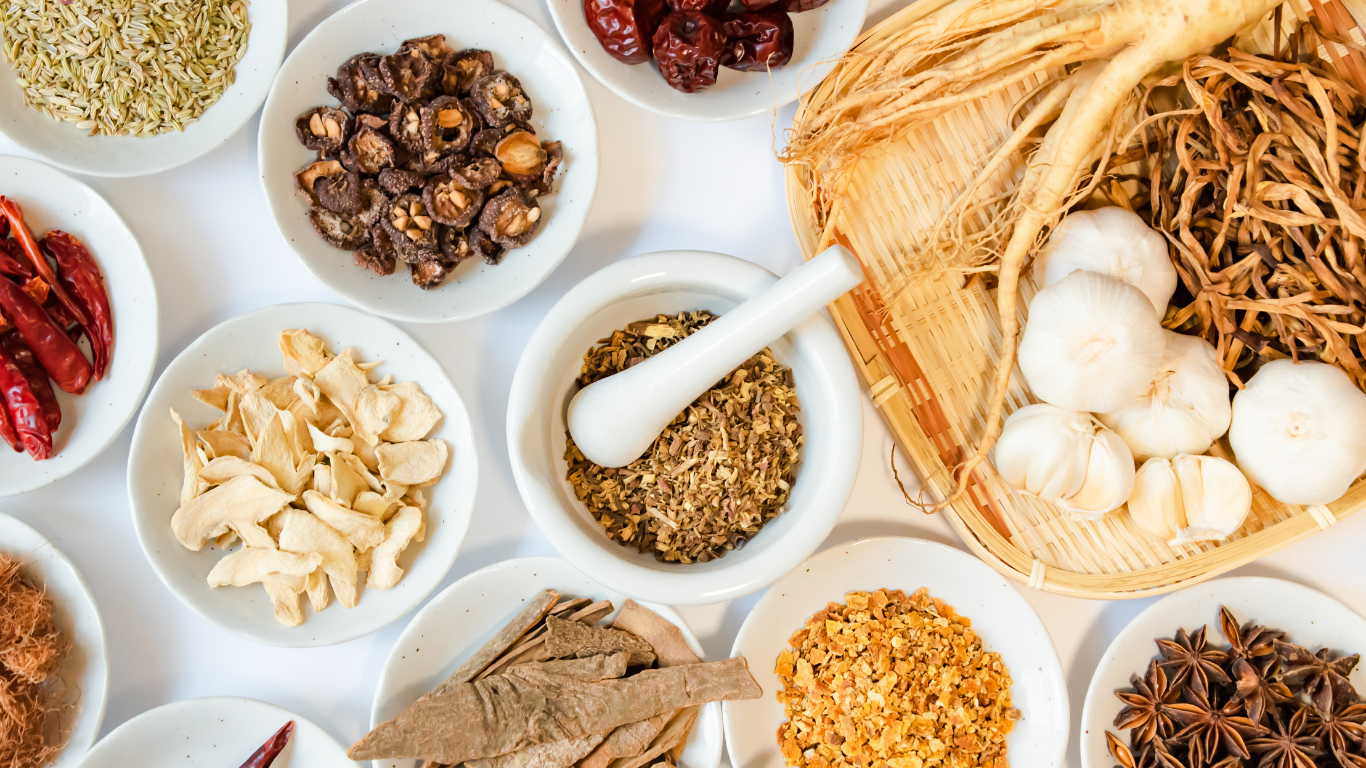 Assorted dried herbs, spices, and garlic in white bowls with a spoon and woven basket