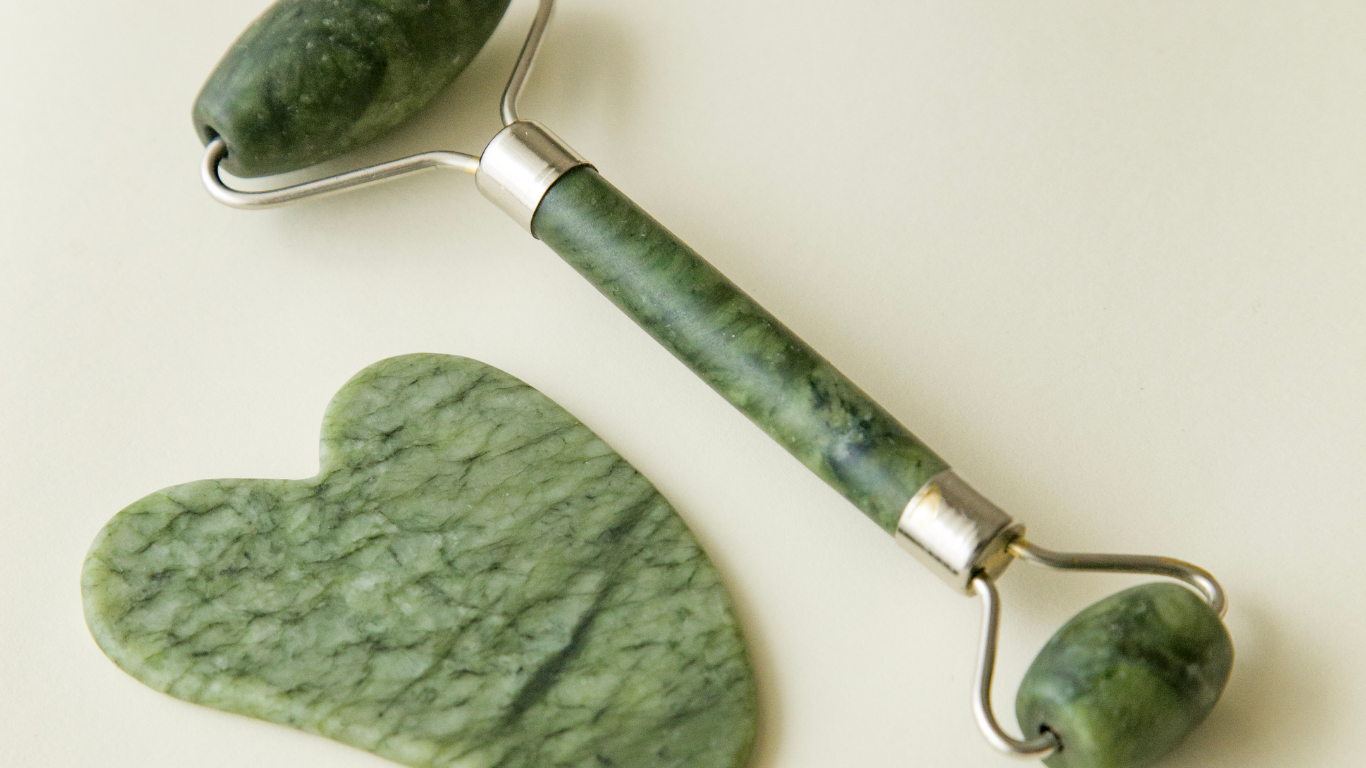 Green jade facial roller with a matching heart-shaped stone on a light background