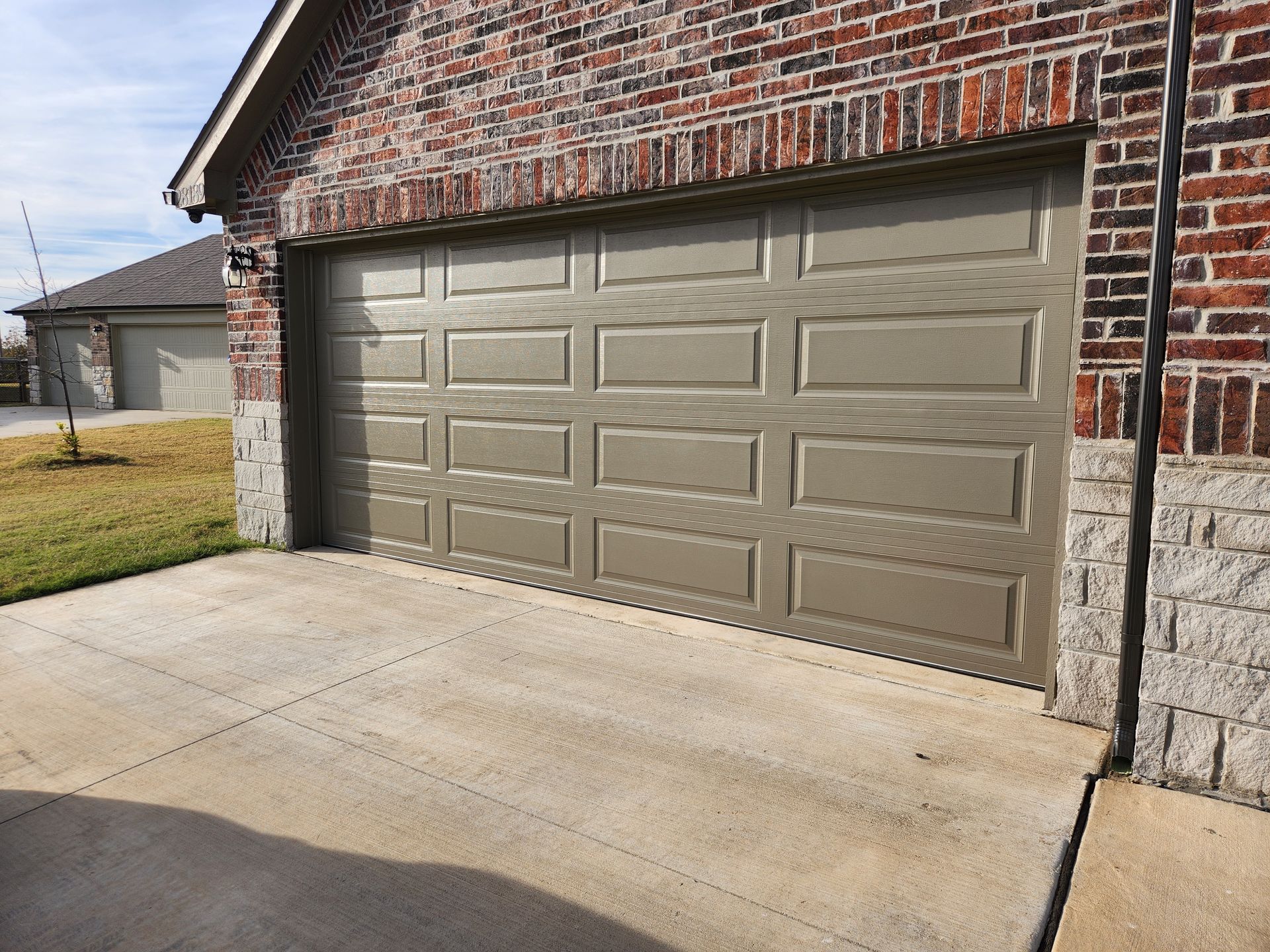 Tan garage door on a brick building with a concrete driveway.