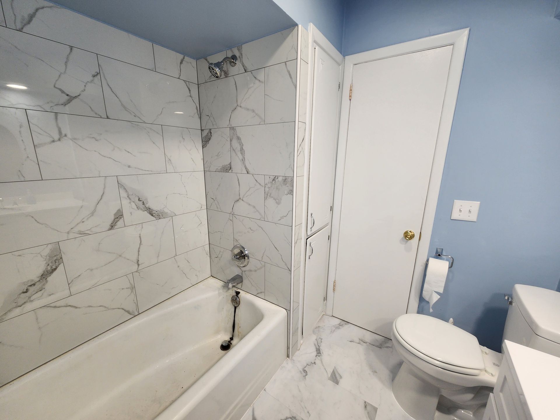 Bathroom with white and gray marble tile, blue walls, and a white toilet.