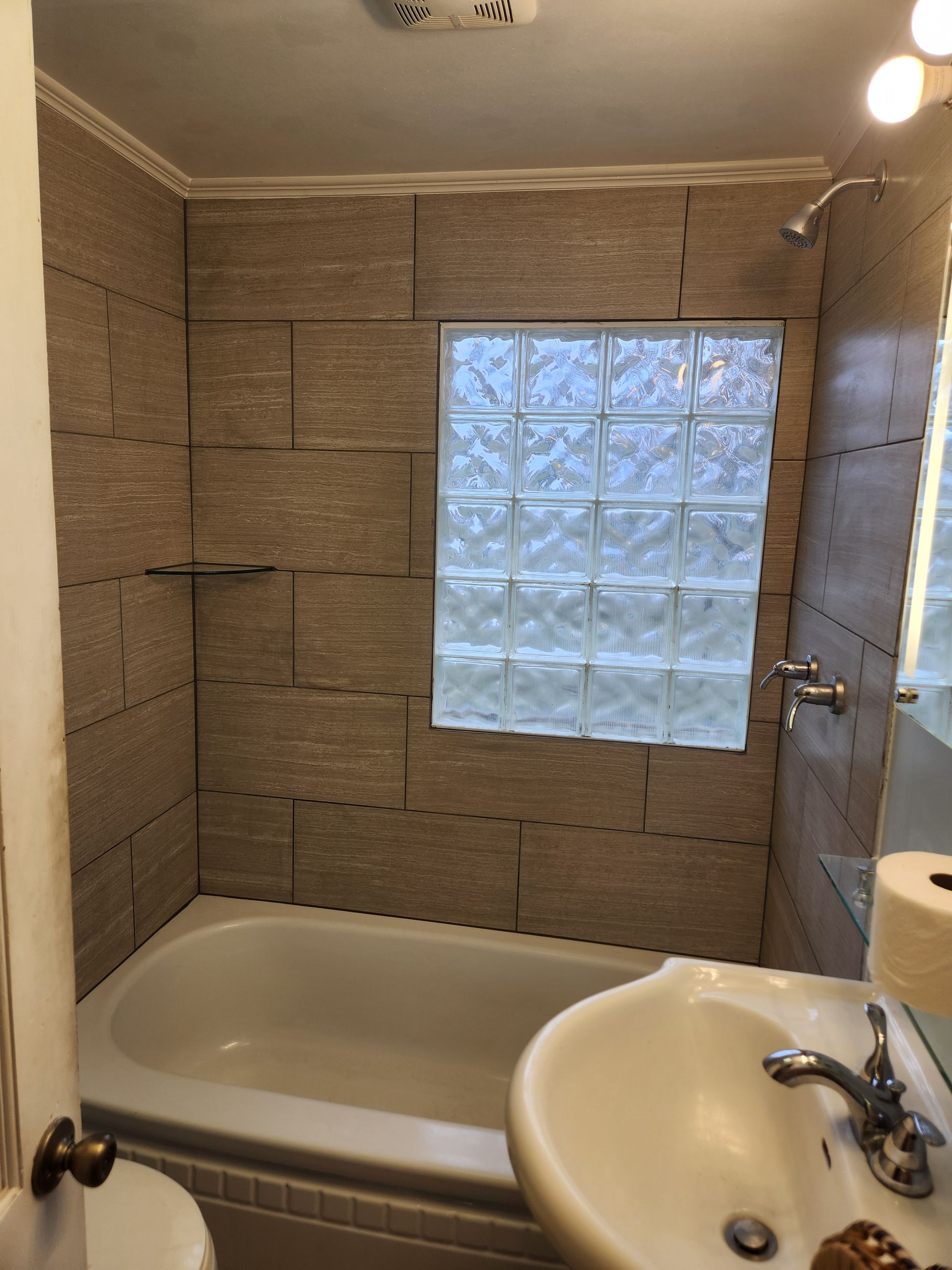 Bathroom with bathtub, sink, and tiled walls. A glass block window is in the shower area.
