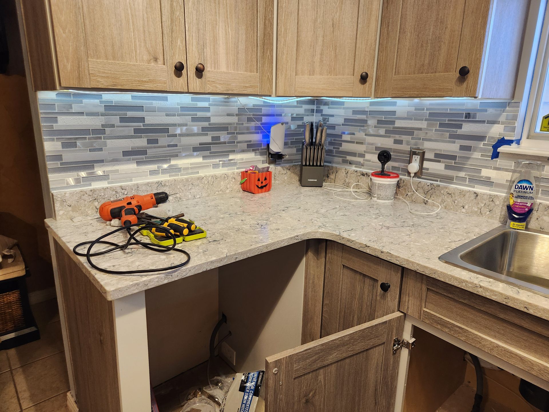 Kitchen renovation with open cabinet, countertop, backsplash, tools, and cabinets.