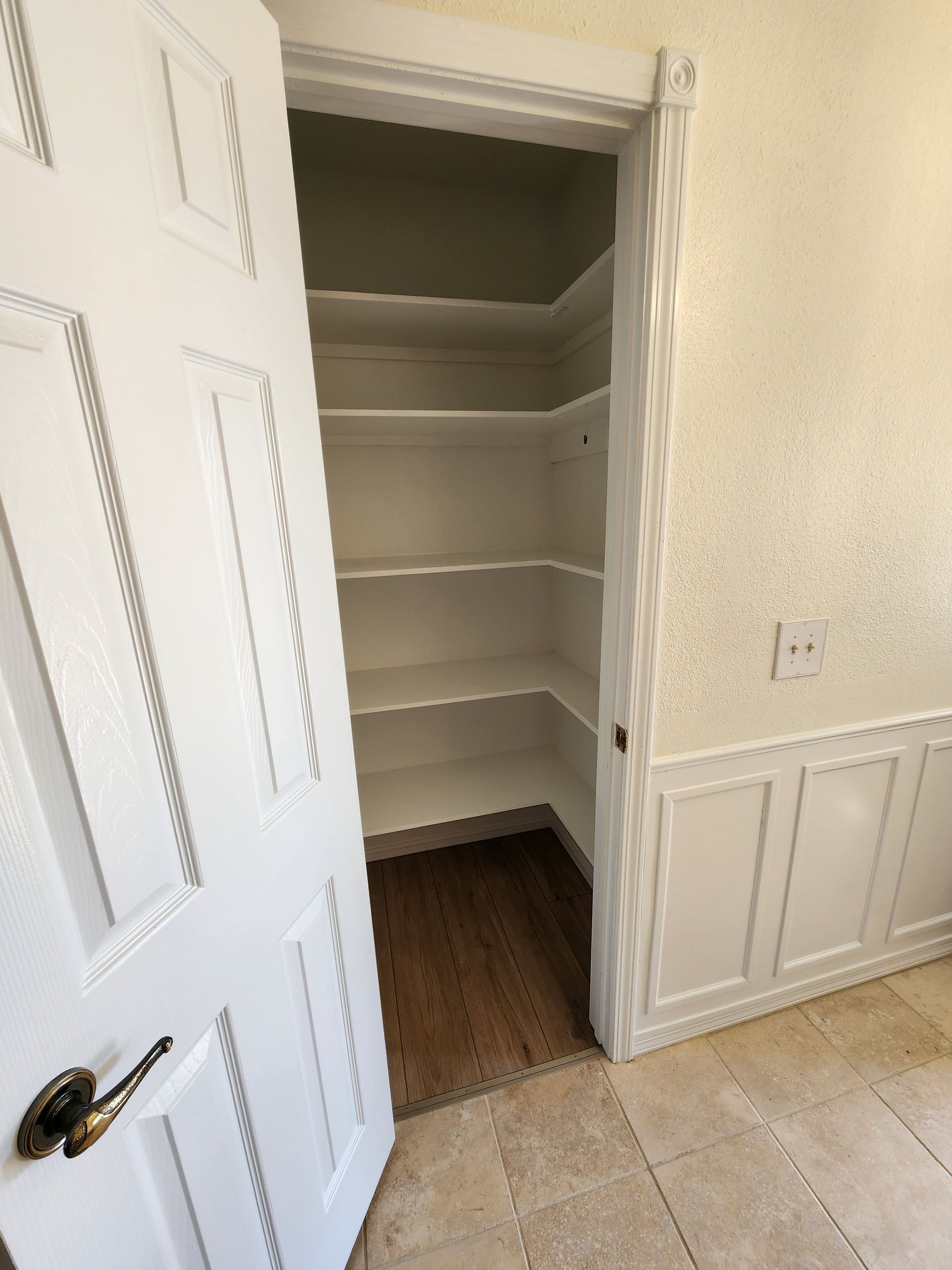 White door open to a pantry with white shelves and a wood floor.