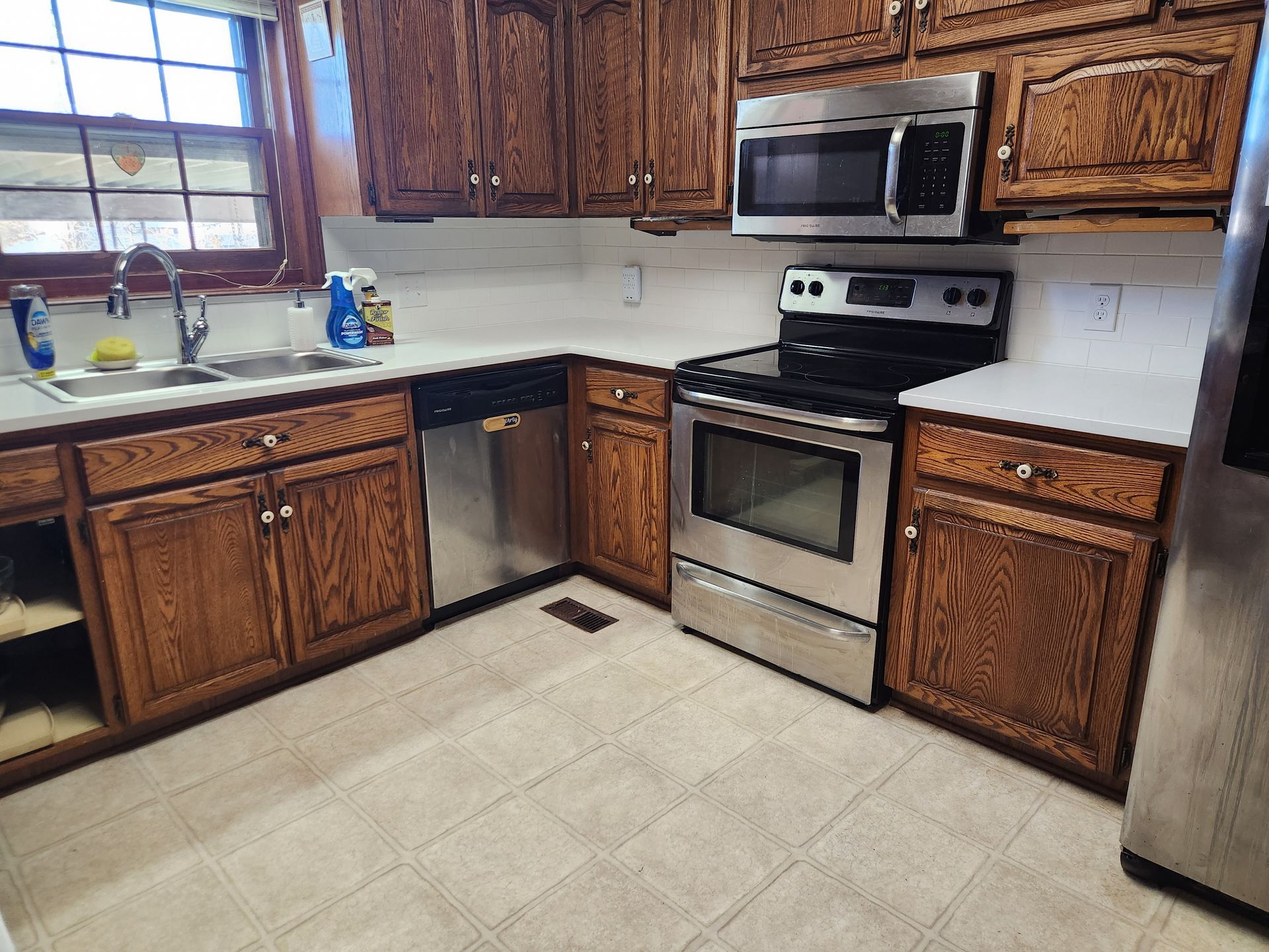 Kitchen with wood cabinets, stainless steel appliances, white countertops, and a window.