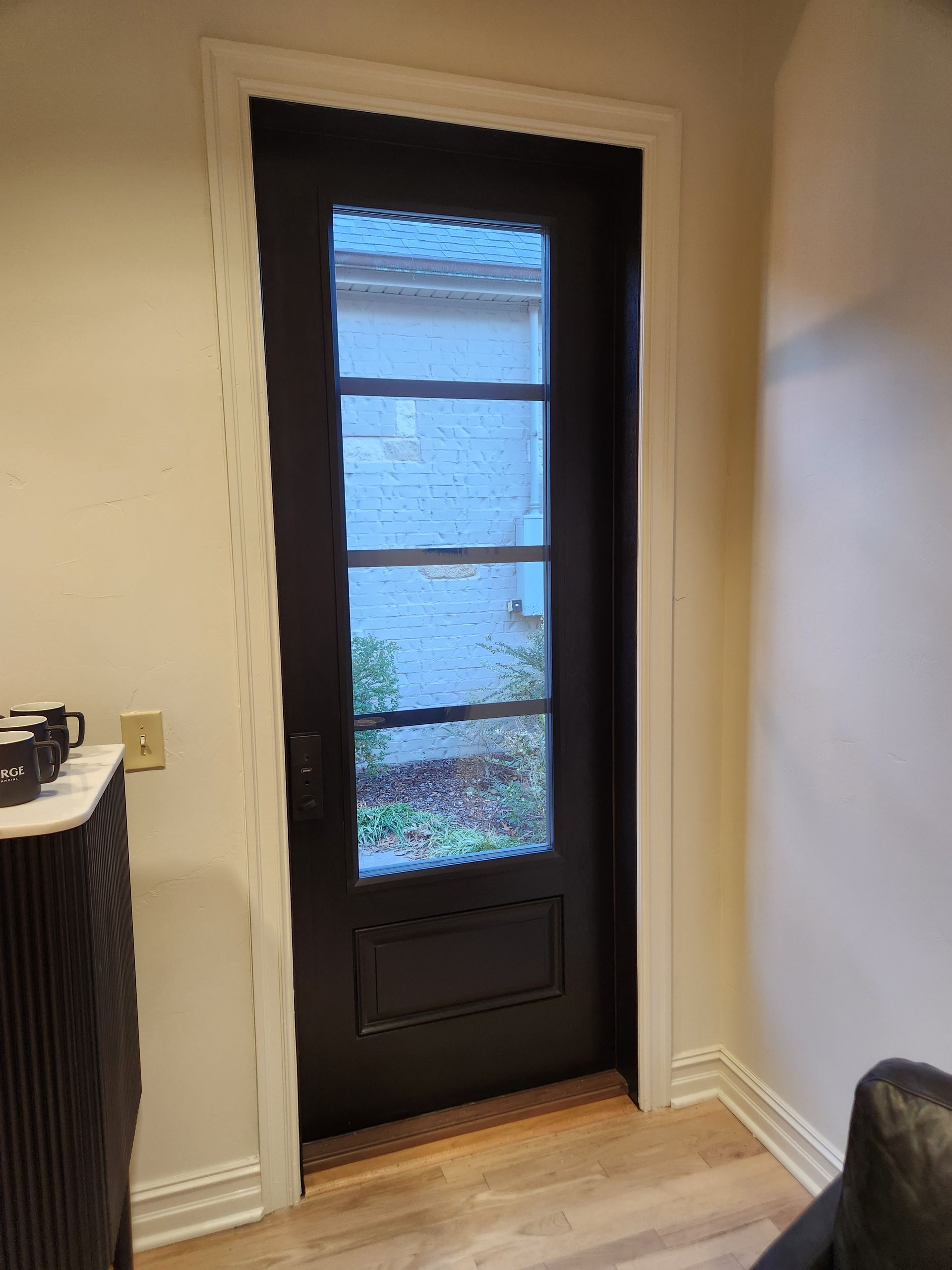 Black door with glass panes in a white-framed doorway, in a room with light beige walls and light wood floor.
