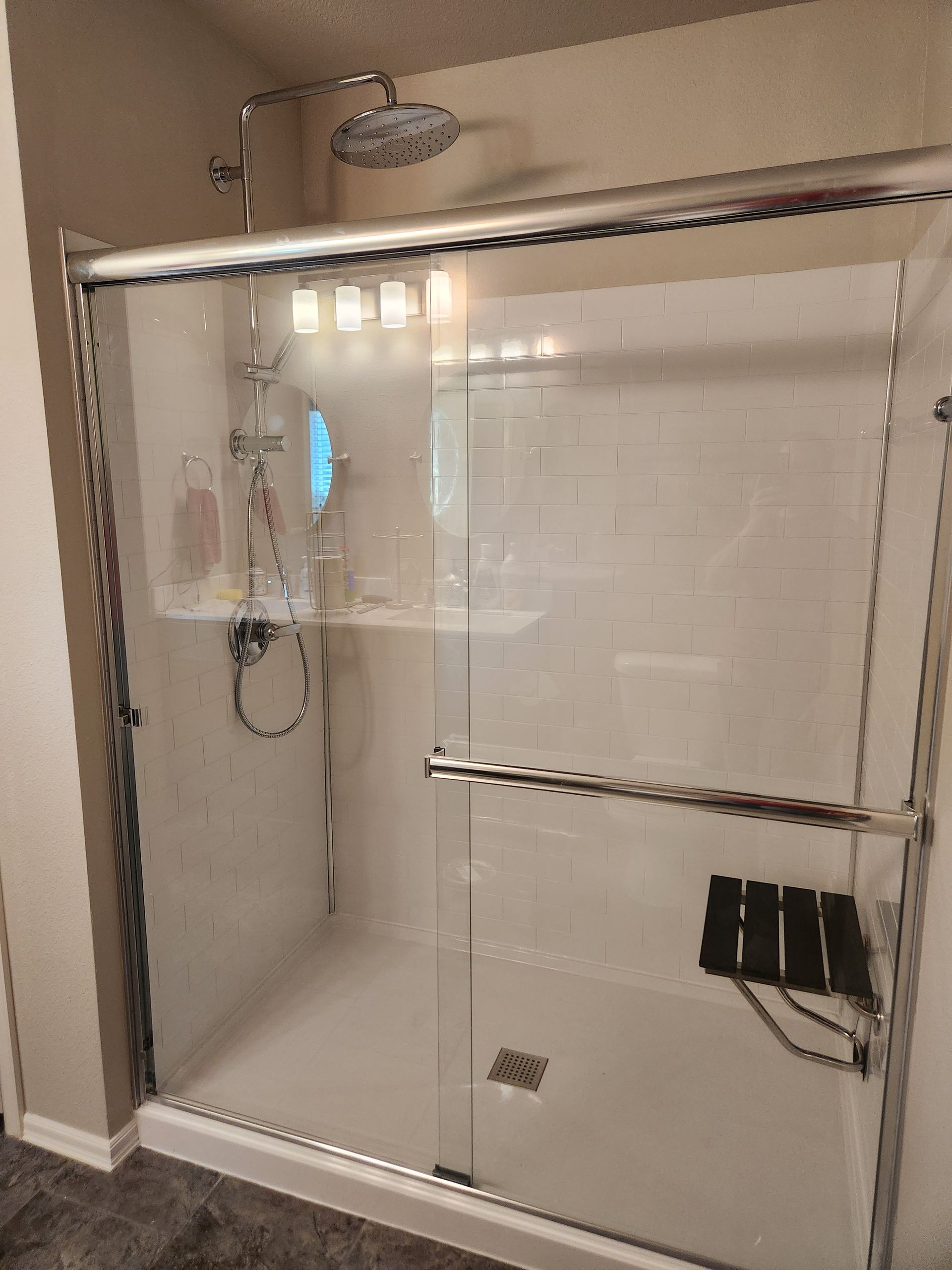 Glass-enclosed shower with sliding doors, silver fixtures, a built-in seat, and a shower head.