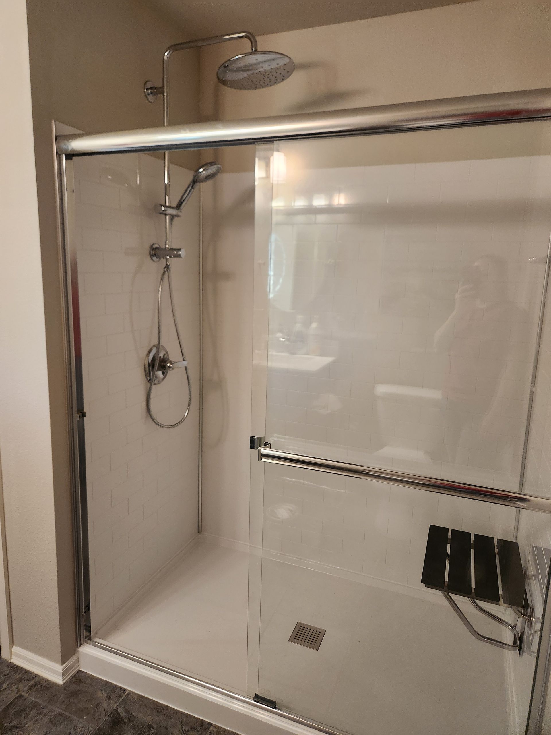 Shower with sliding glass doors, a handheld showerhead, a seat, and a rainfall showerhead.