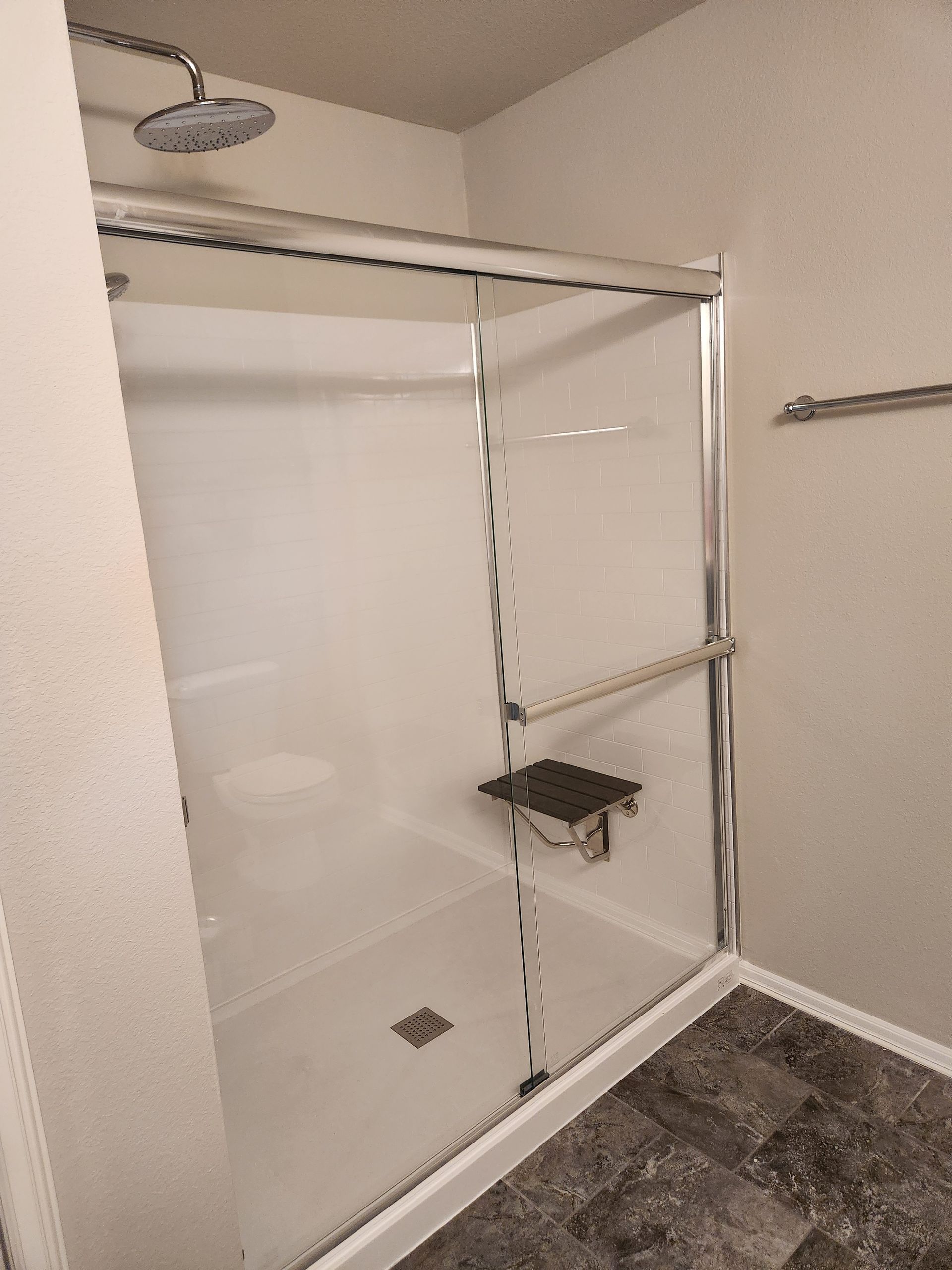 A walk-in shower with a seat, glass doors, and a rain showerhead. Gray tile floor.