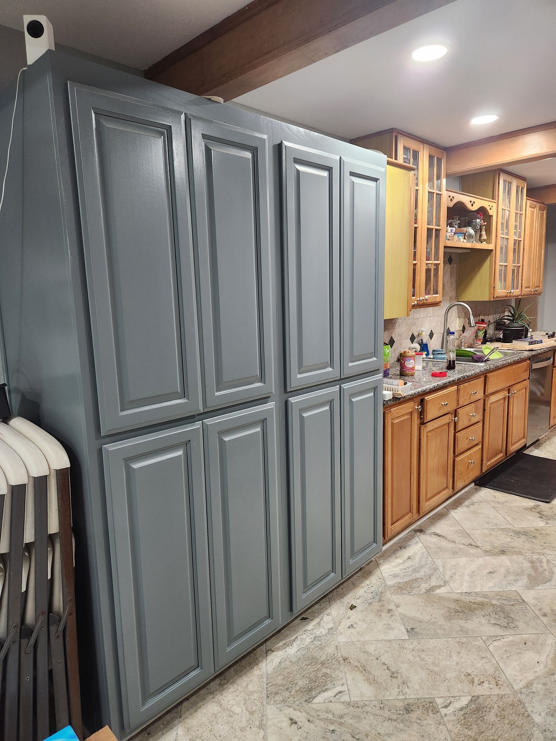 Tall gray cabinets next to light wood cabinets in a kitchen with a concrete floor.