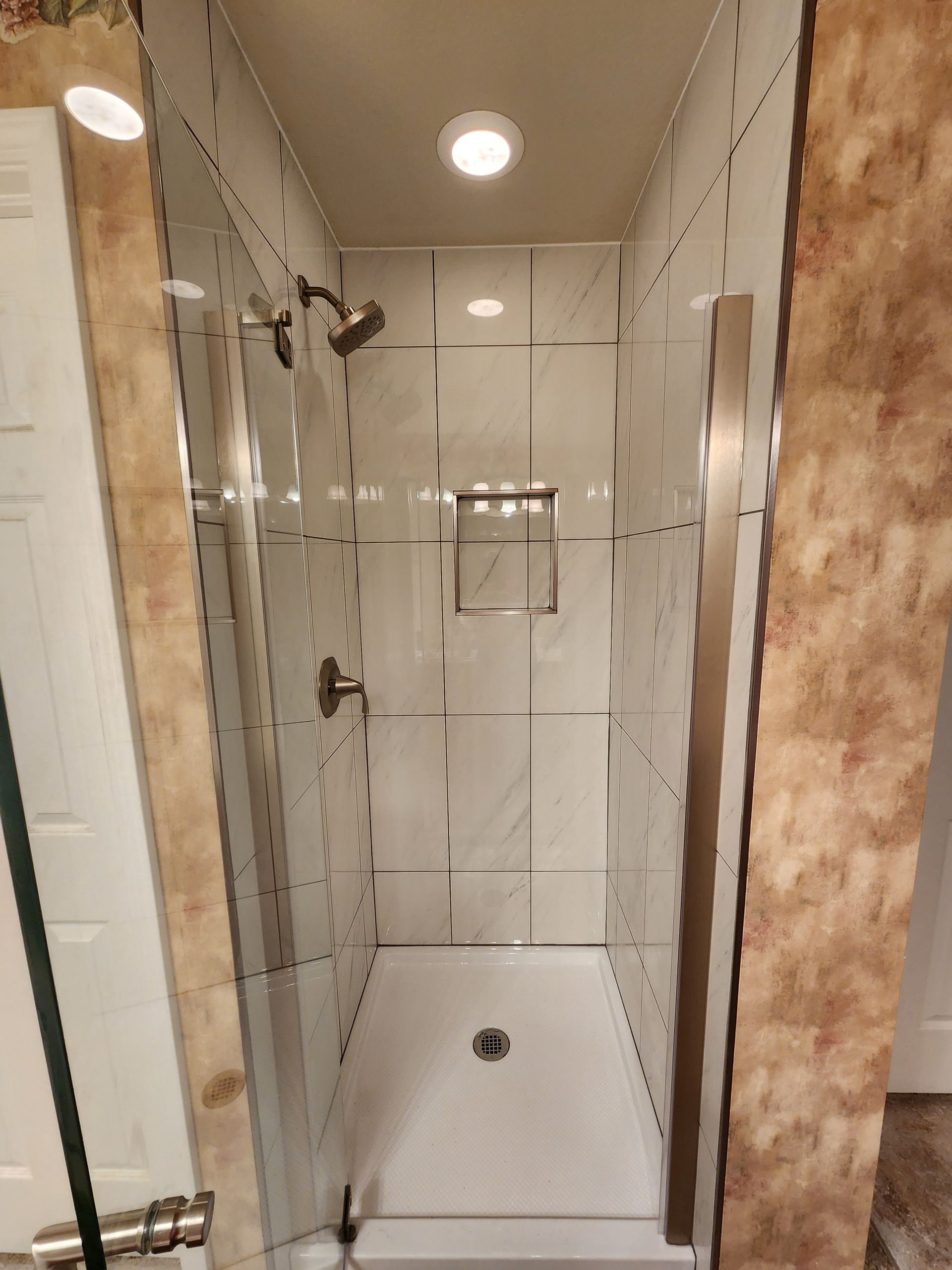 Shower with white tiled walls, glass doors, and a recessed shelf.