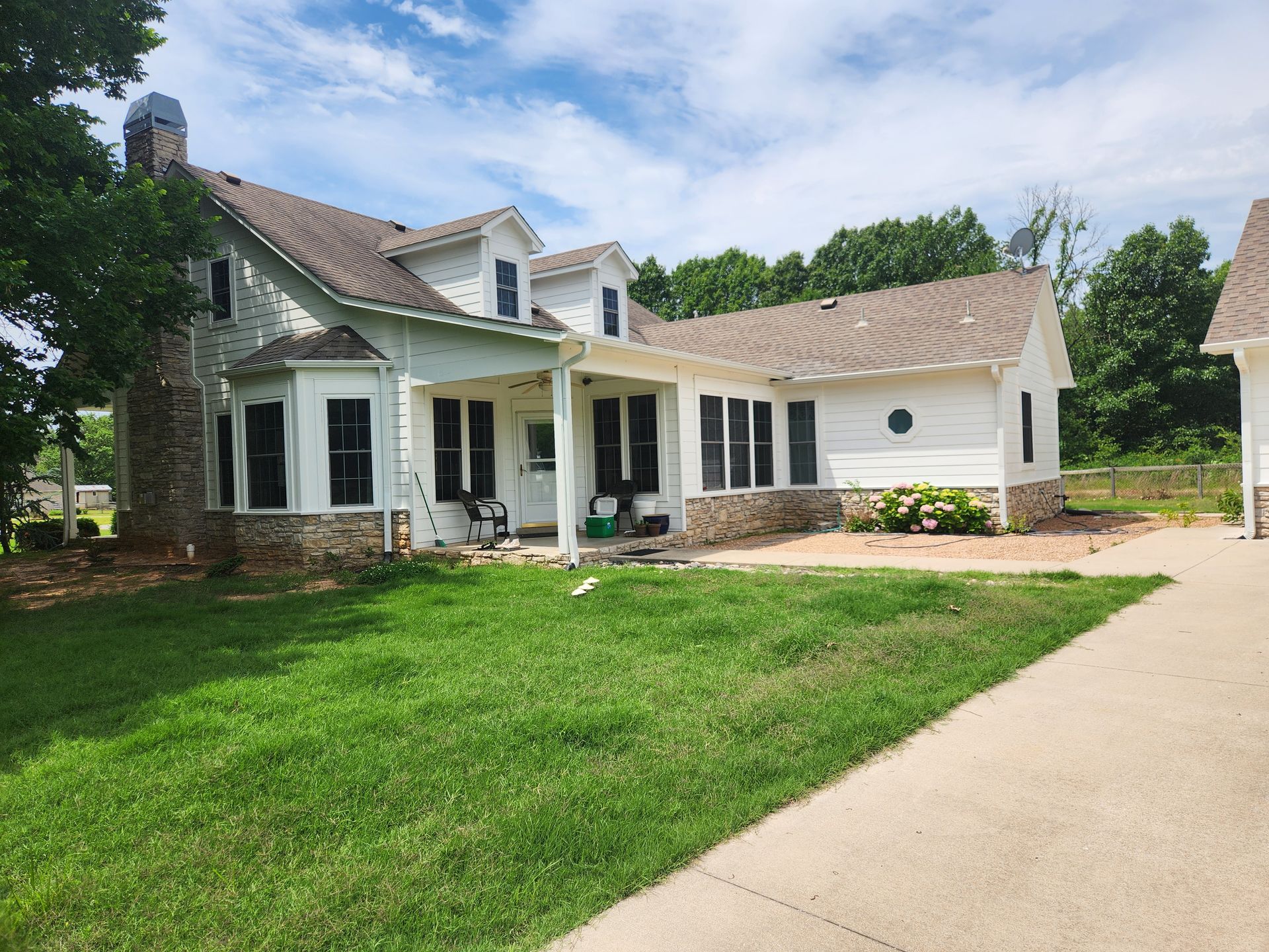 White house with stone accents, a porch, and a brown roof against a blue sky.