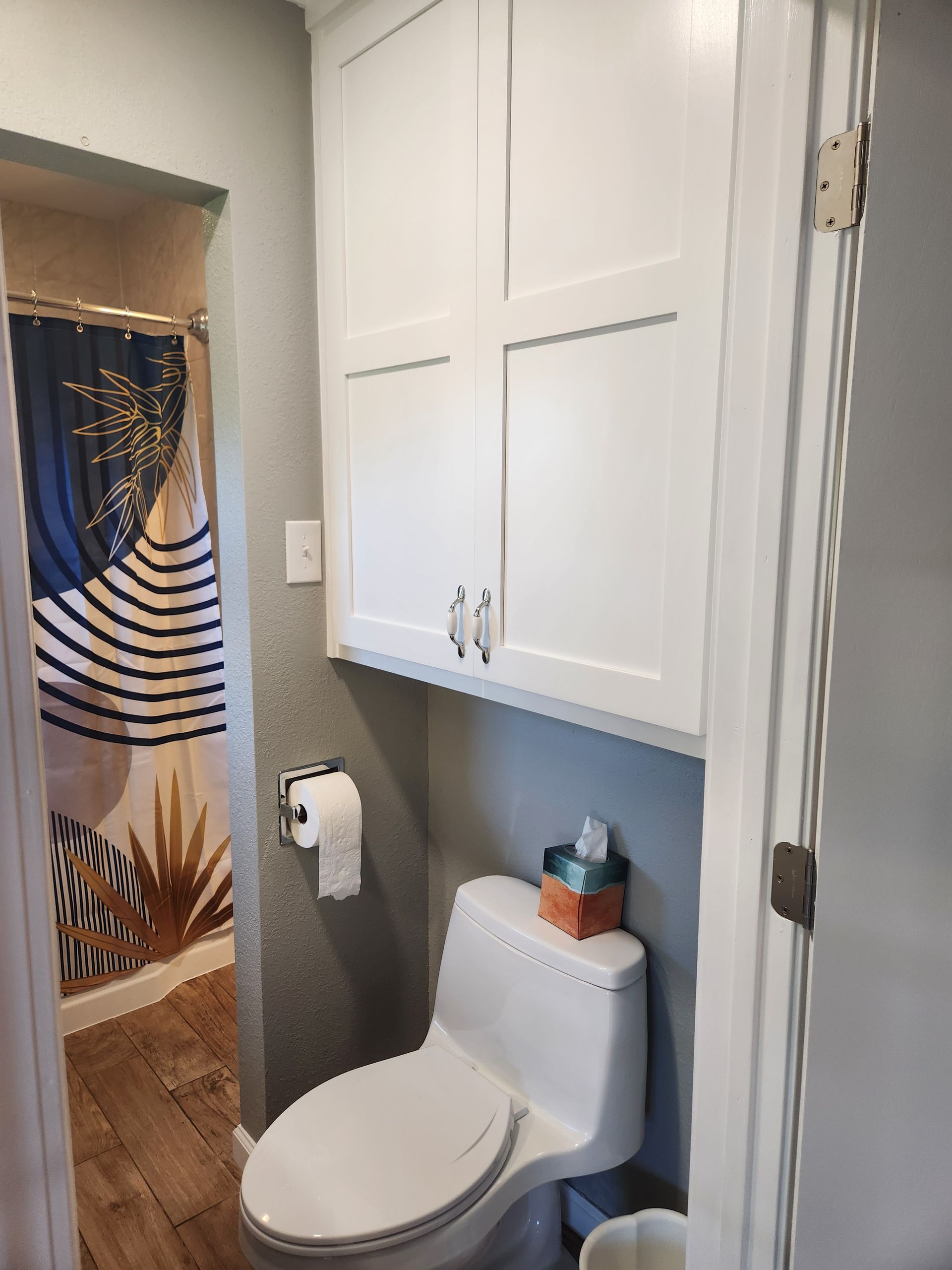 Small bathroom with white cabinets above the toilet and a shower stall visible in the doorway.