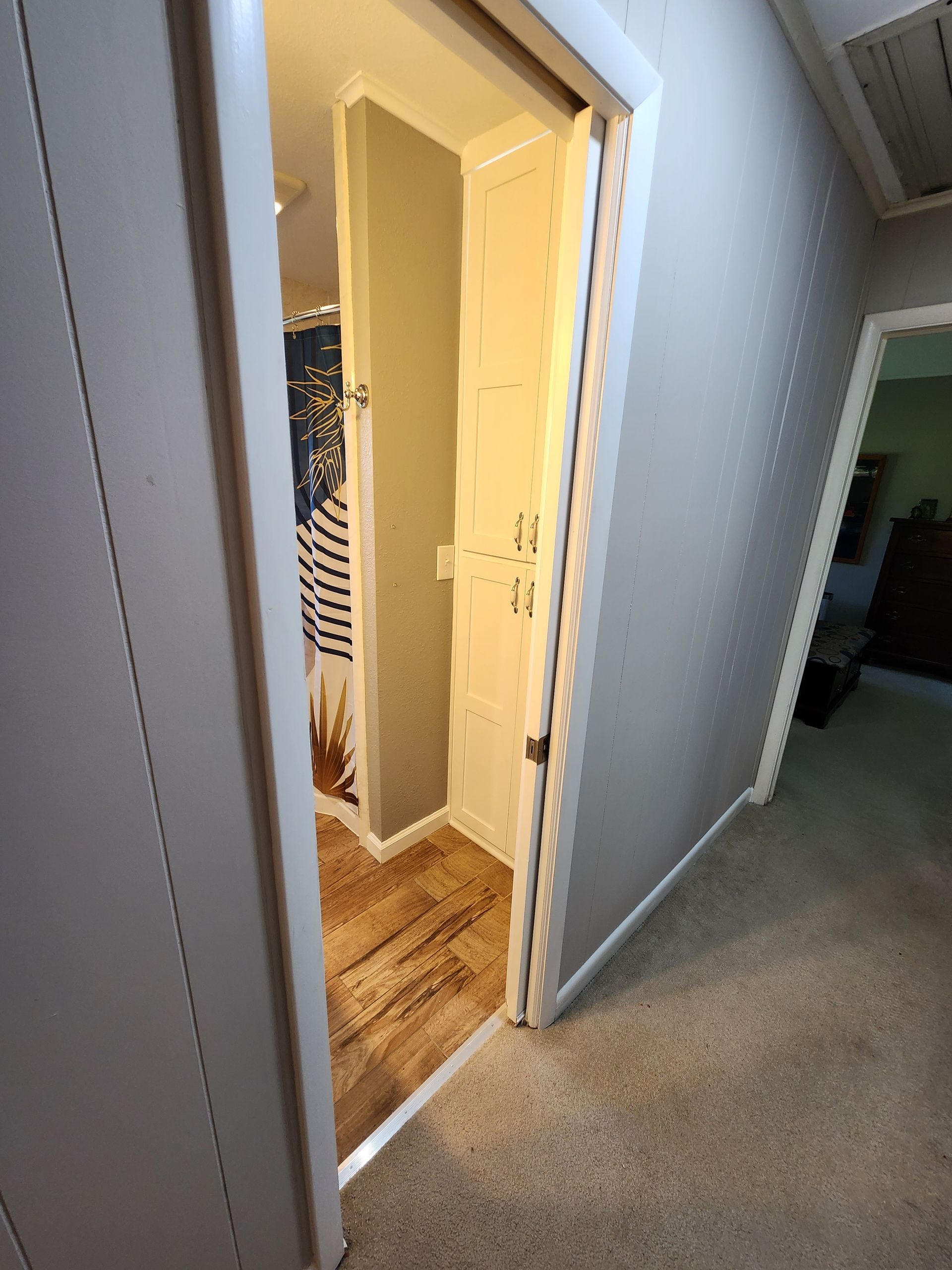 Hallway with a doorway leading to a narrow bathroom and closet with a white trim and doors.