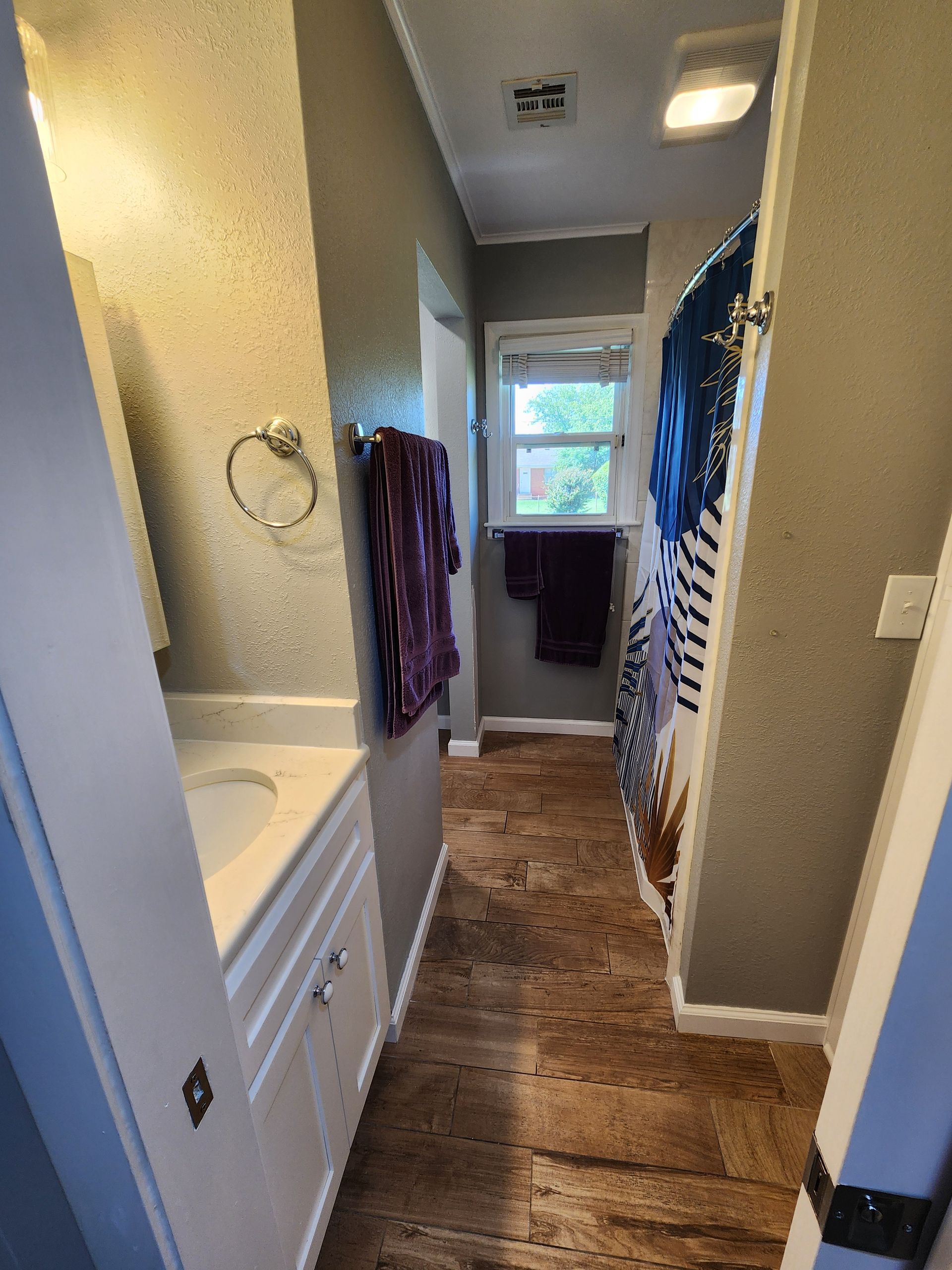 Narrow bathroom with white vanity, gray walls, wood-look floor, and shower curtain.