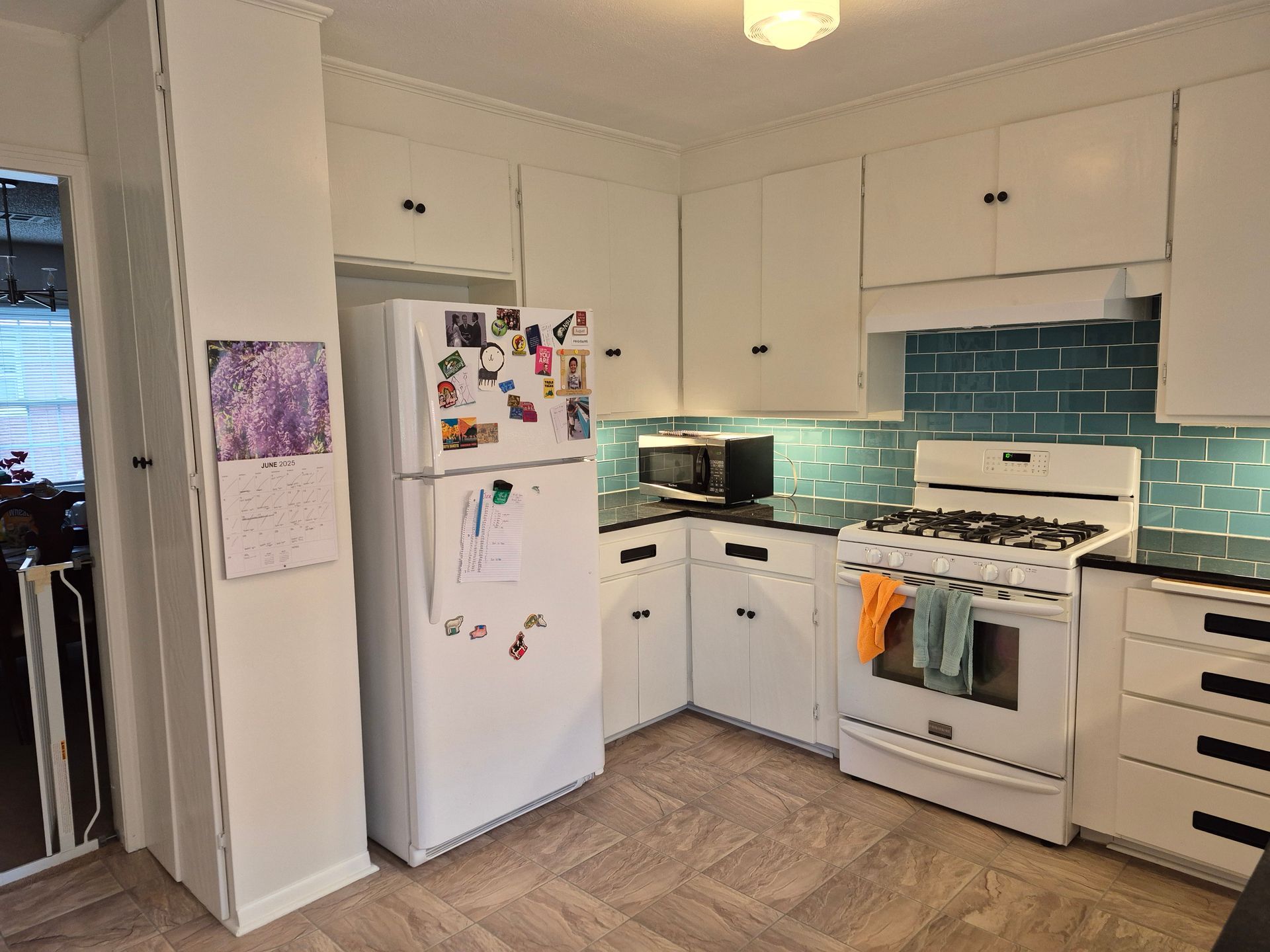 White kitchen with white cabinets, turquoise backsplash, and a white refrigerator.