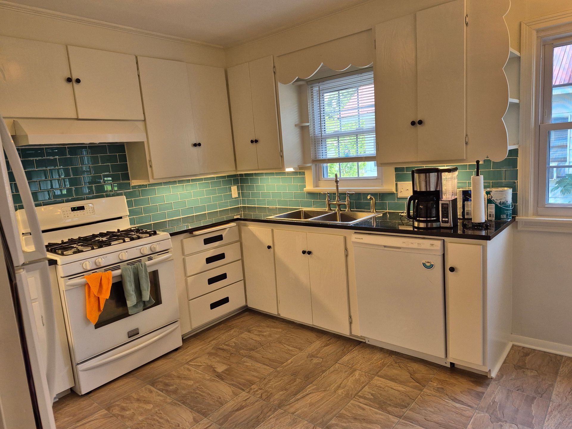 White kitchen with teal backsplash, cabinets, and appliances. Wooden floor.