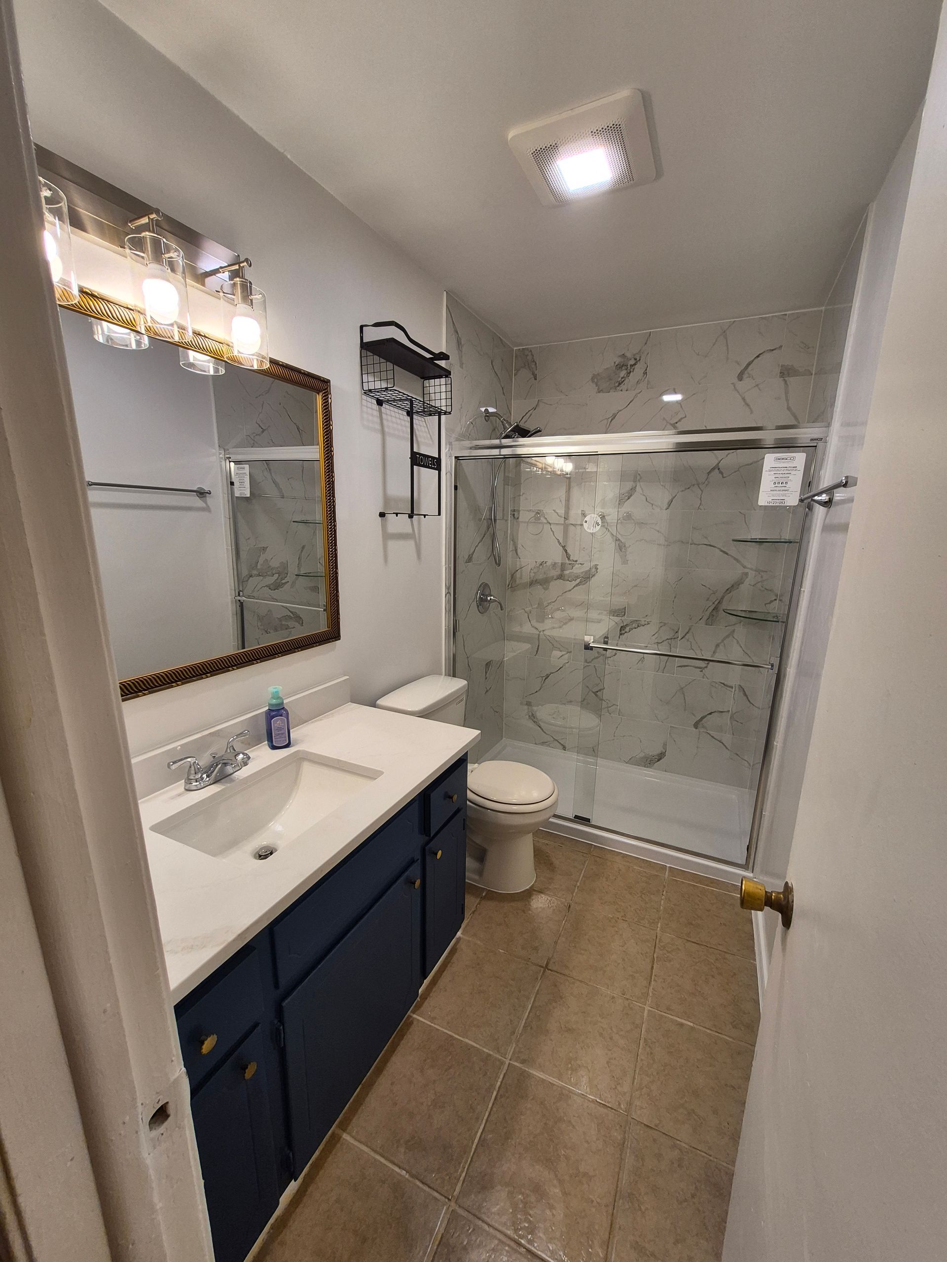 Bathroom with blue vanity, white sink, beige tile floor, and a glass shower.