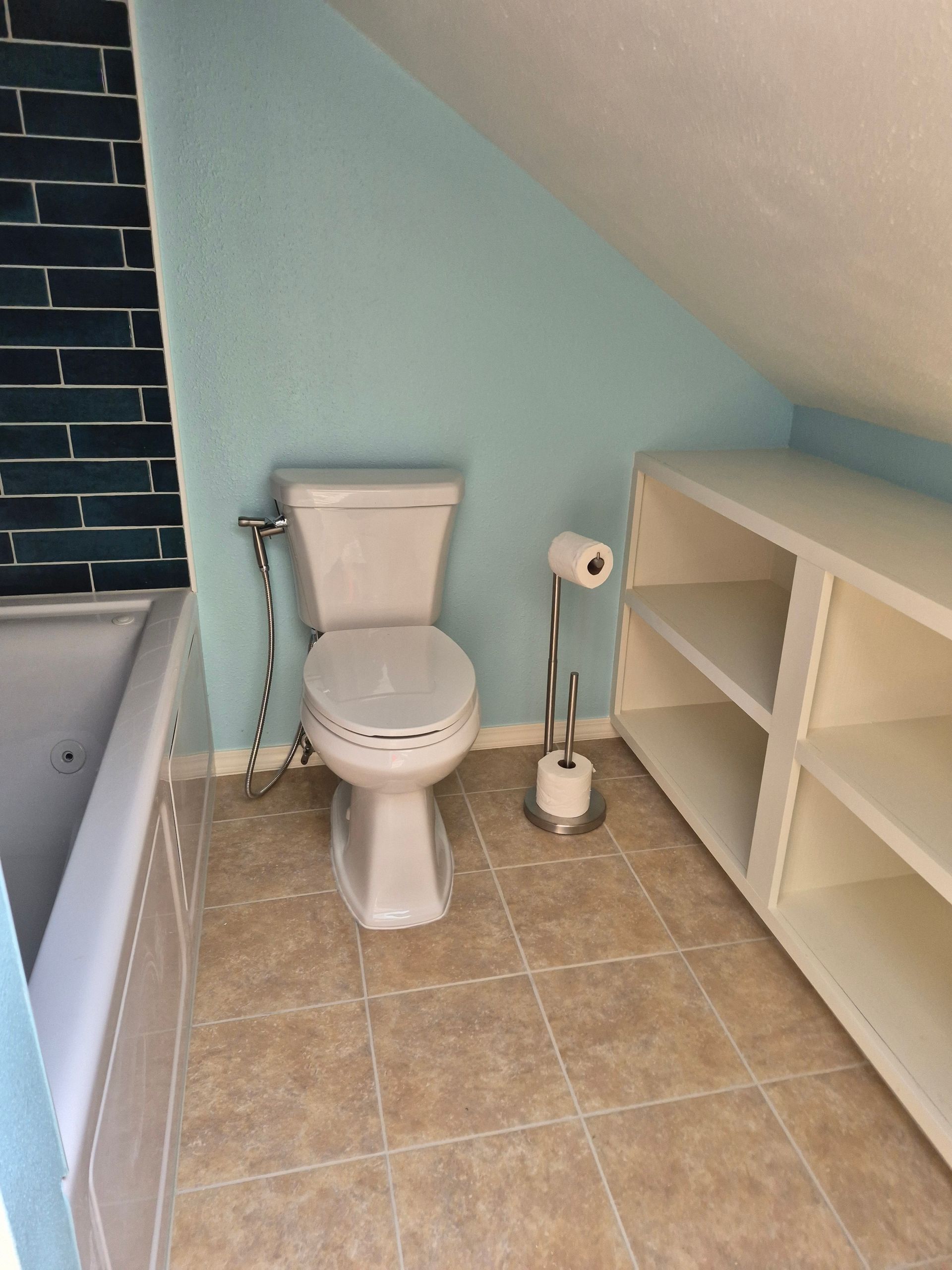 Bathroom with toilet, built-in shelves, and blue and white walls under a slanted ceiling.