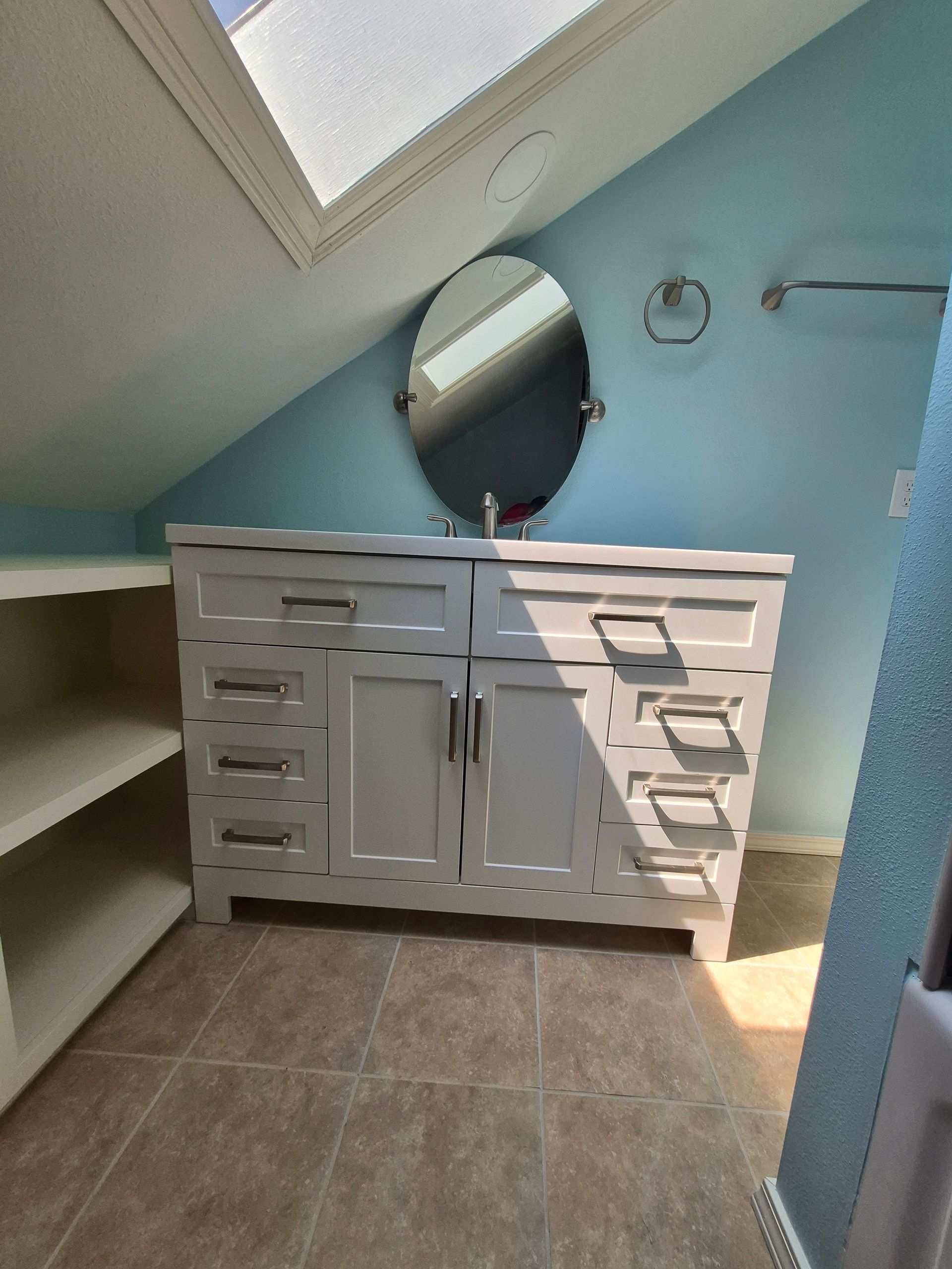 Bathroom with white vanity, oval mirror, and blue walls. Skylight overhead.
