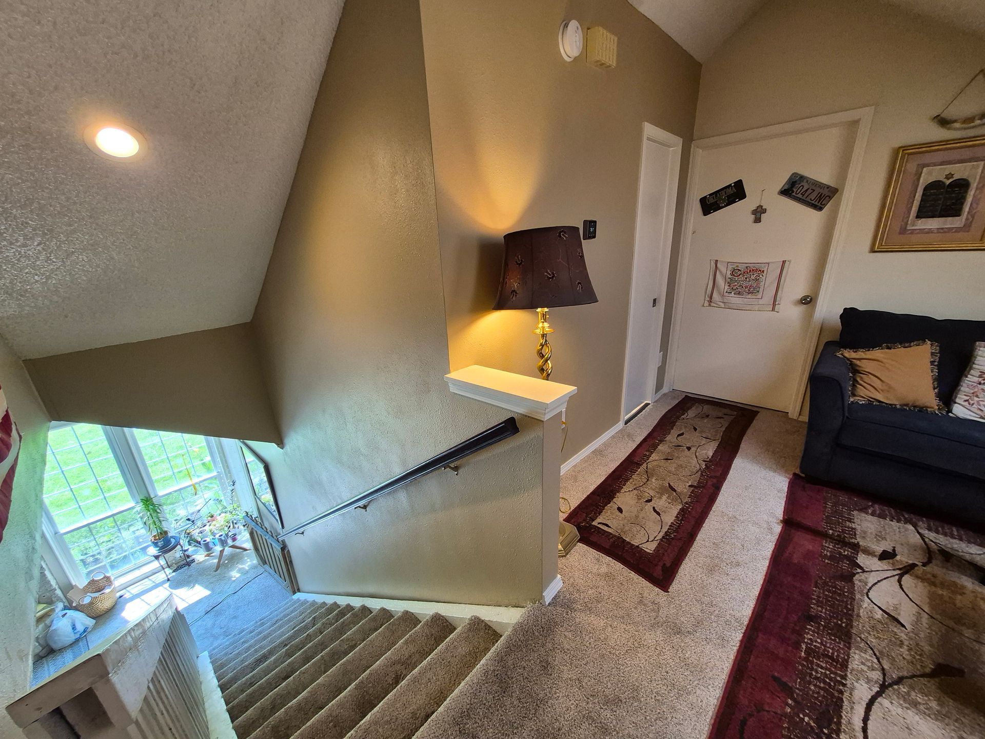 Staircase with carpet, handrail, and wall lamp. Hallway leads to door and rug.