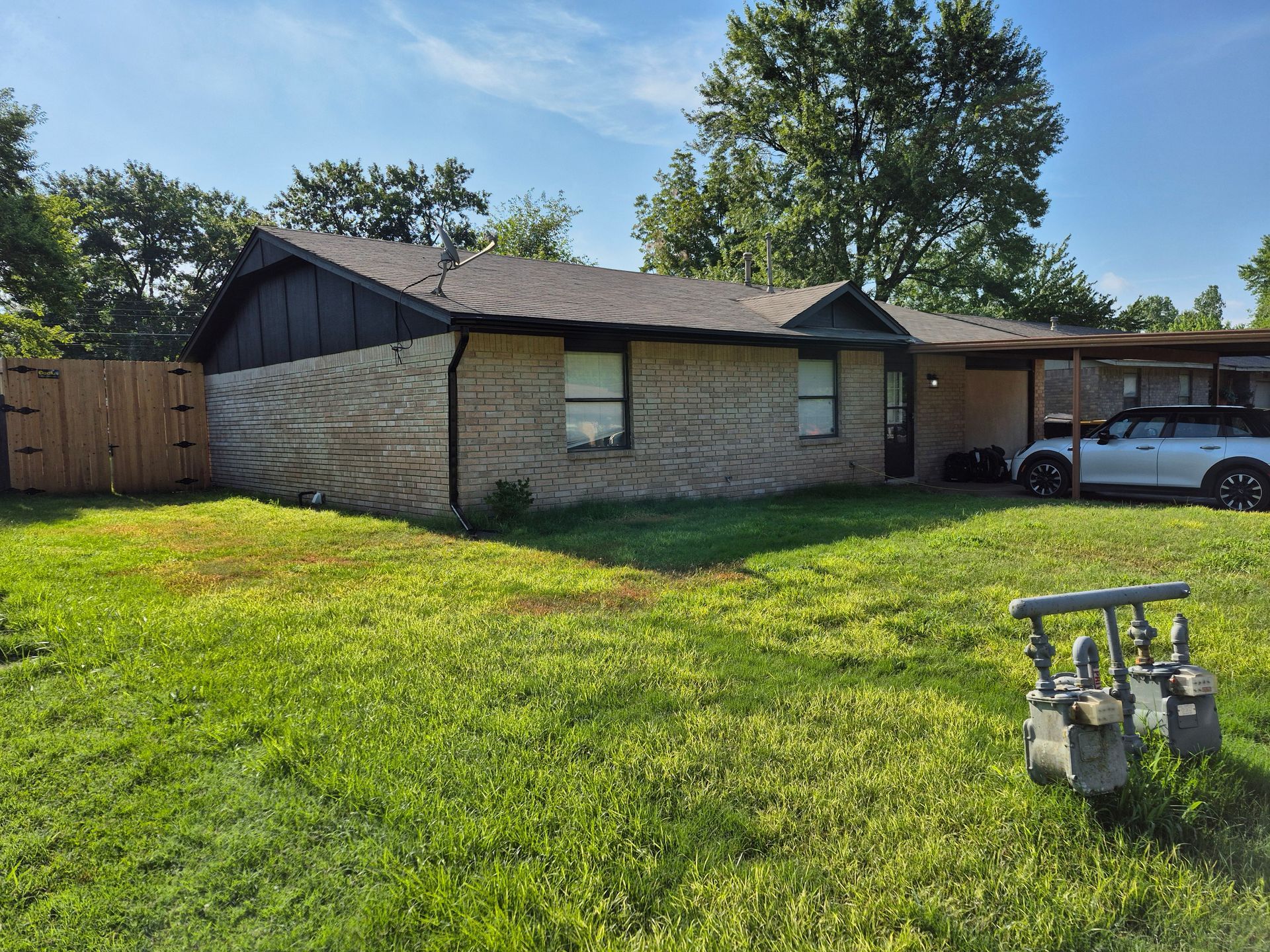 Brick ranch home with a car under a carport, green lawn, and wooden fence.