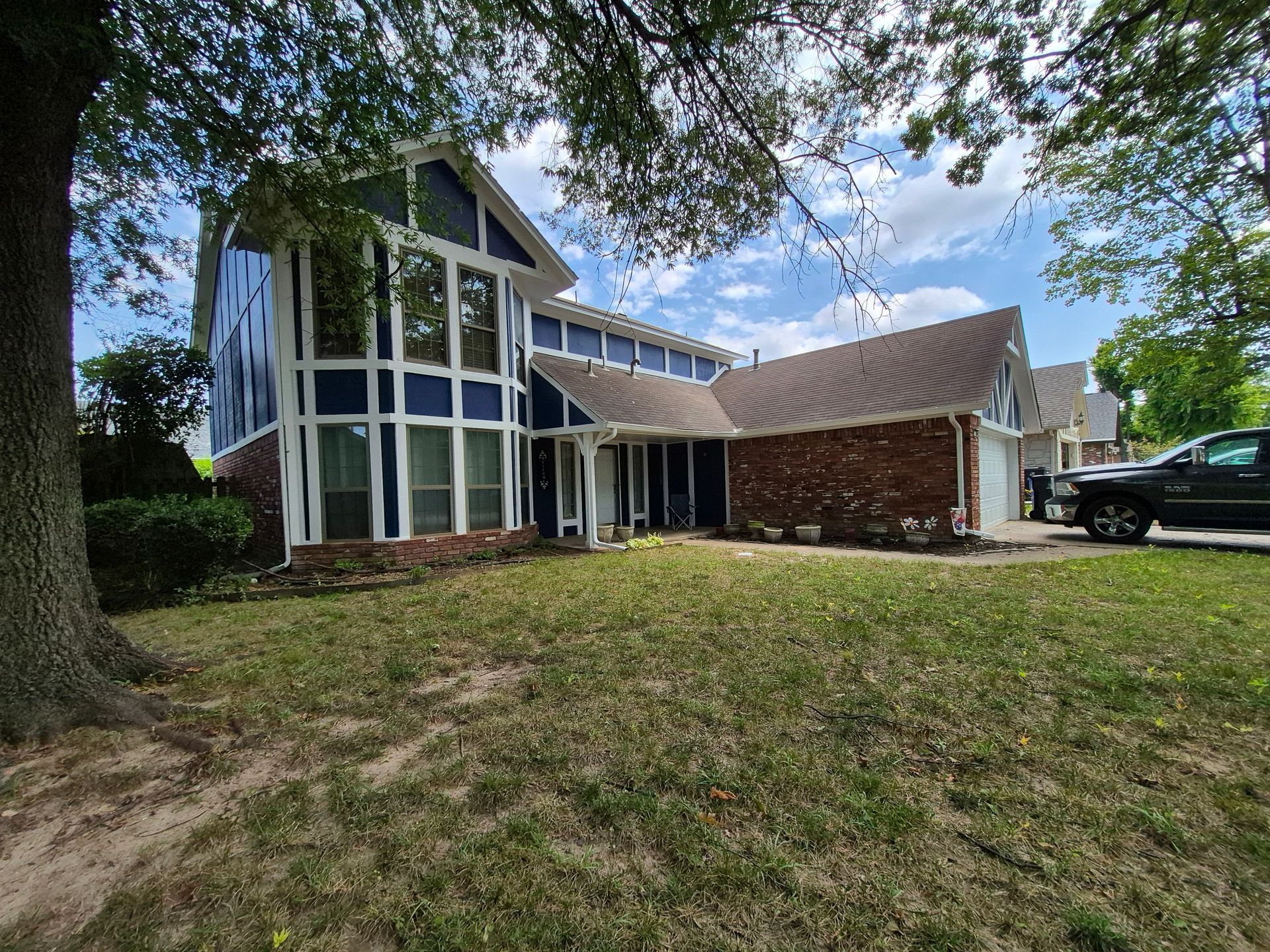 Blue and brick house with large windows, brown roof, and a green lawn.
