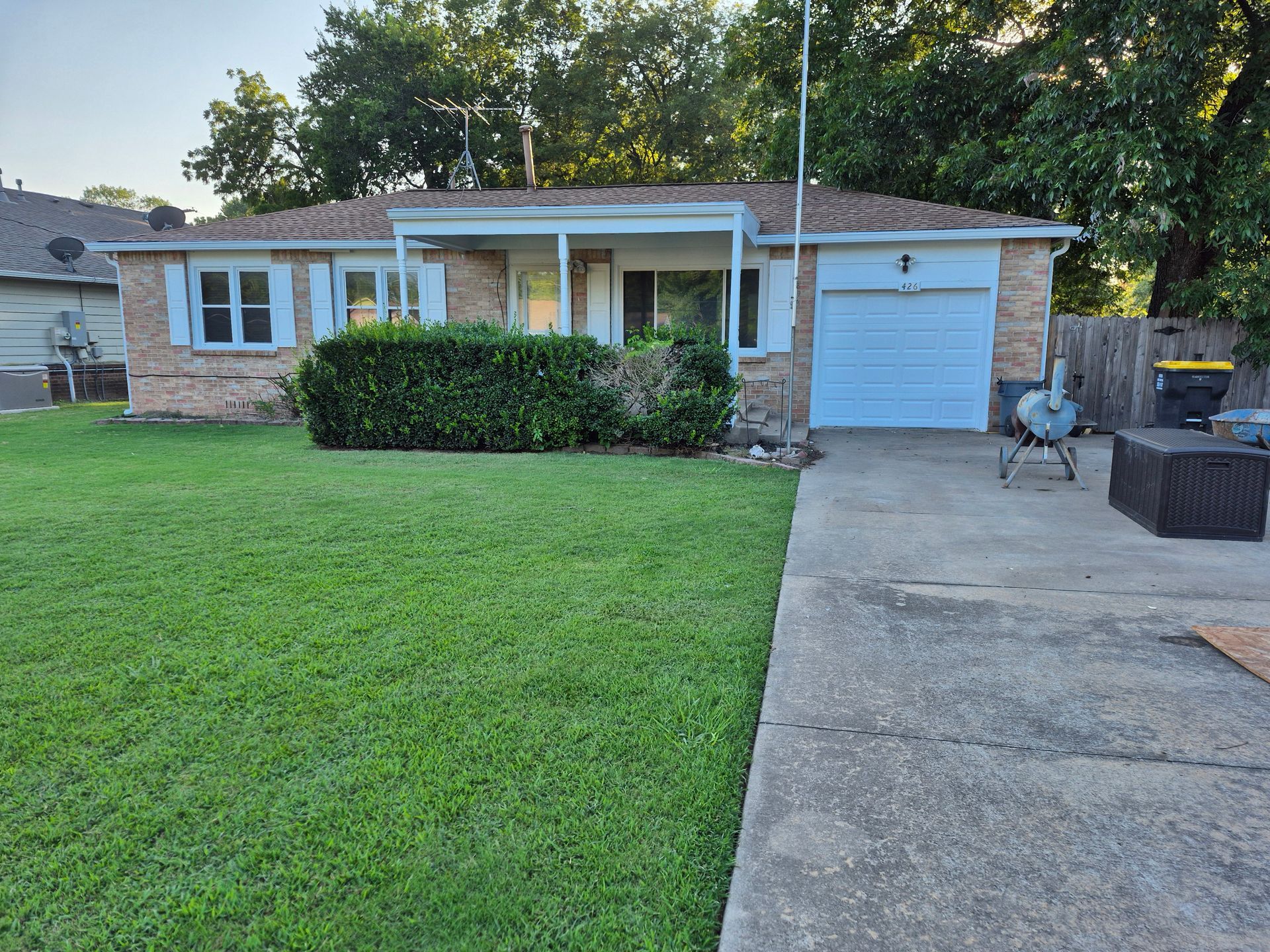 Brick house with green lawn, driveway, and closed garage door; shrubs in front.