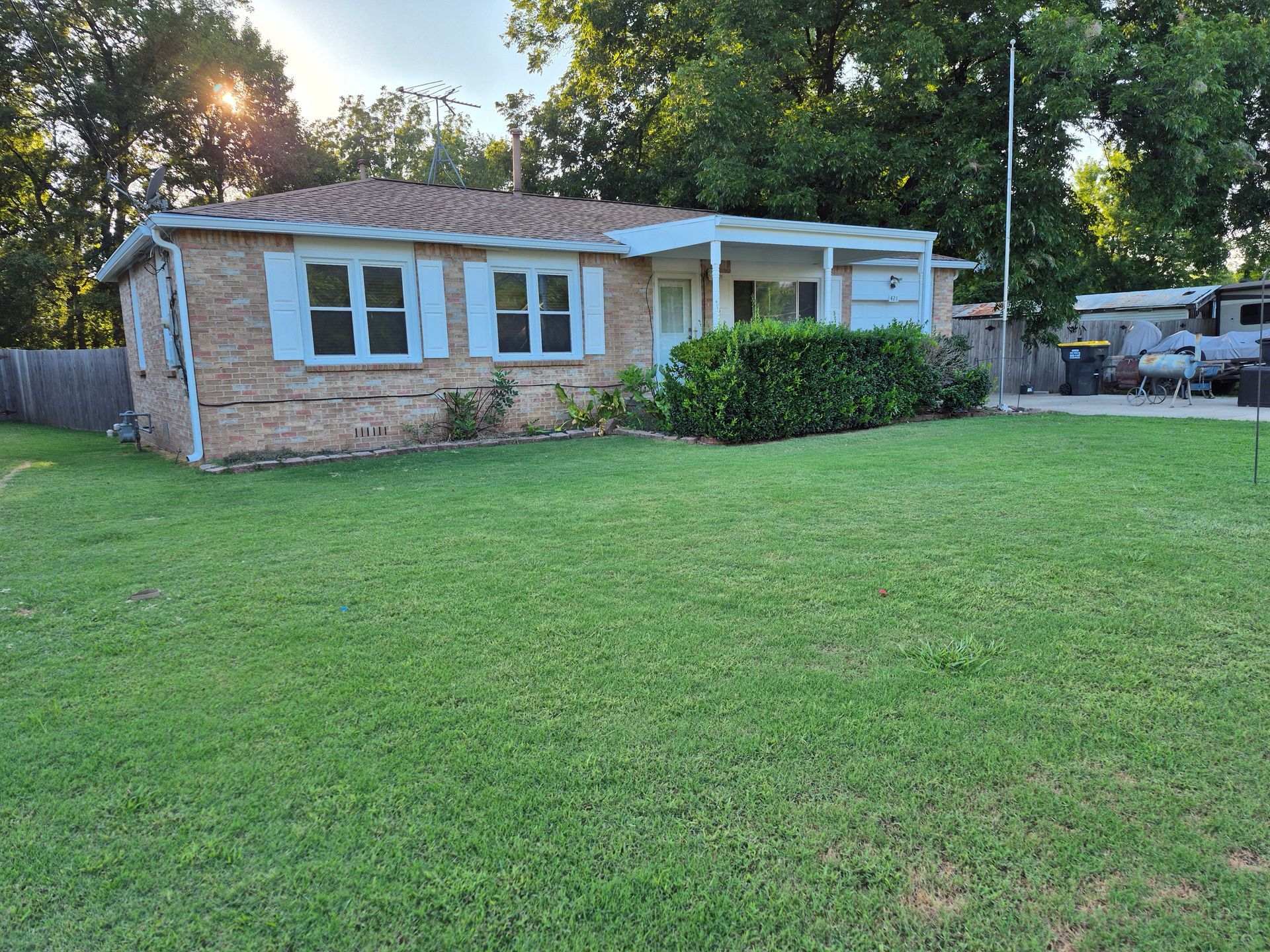 Brick ranch-style house with blue shutters, green lawn, trees, and RV in the background.