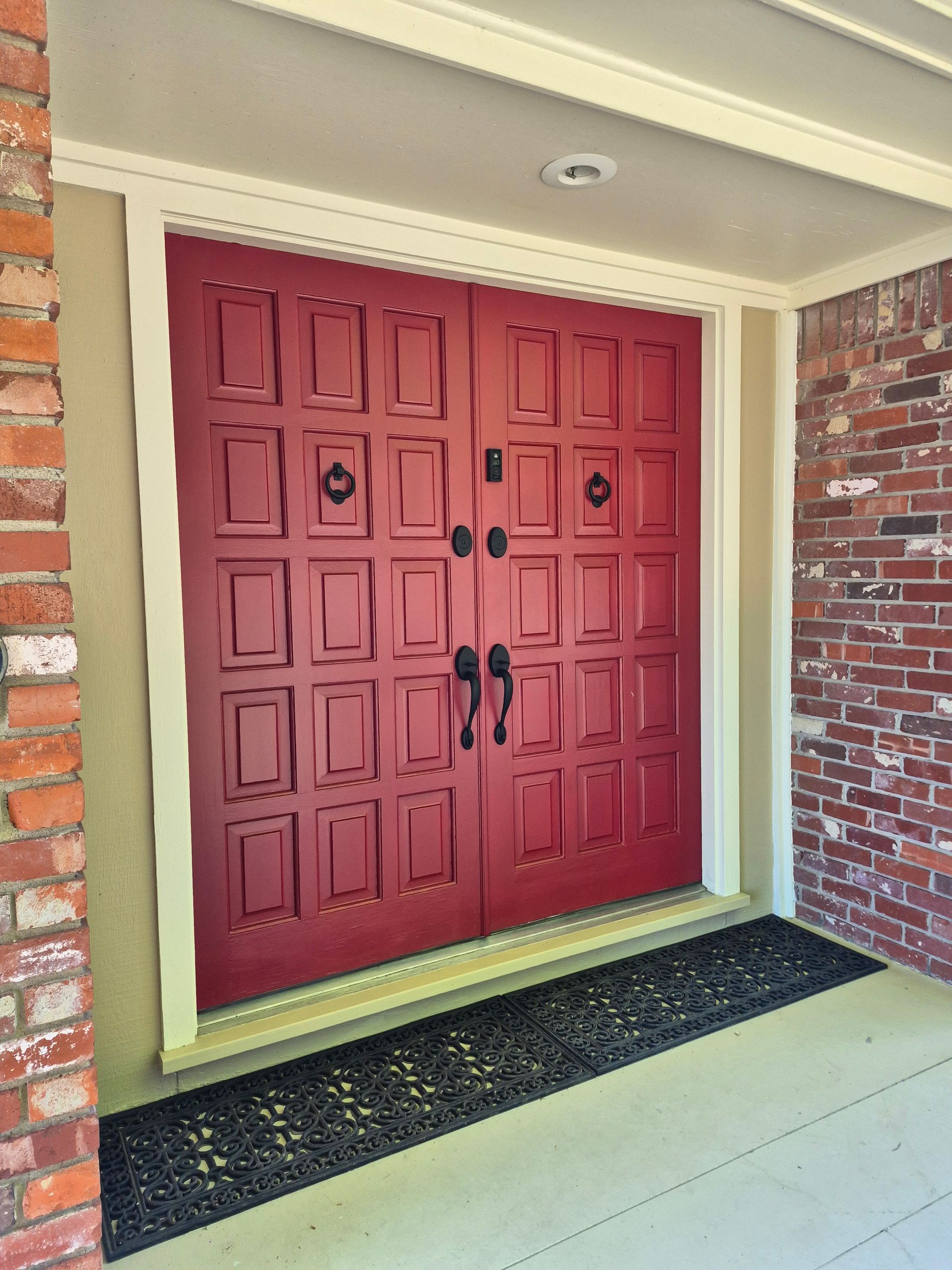 Red double doors with black hardware, framed by brick and light trim.
