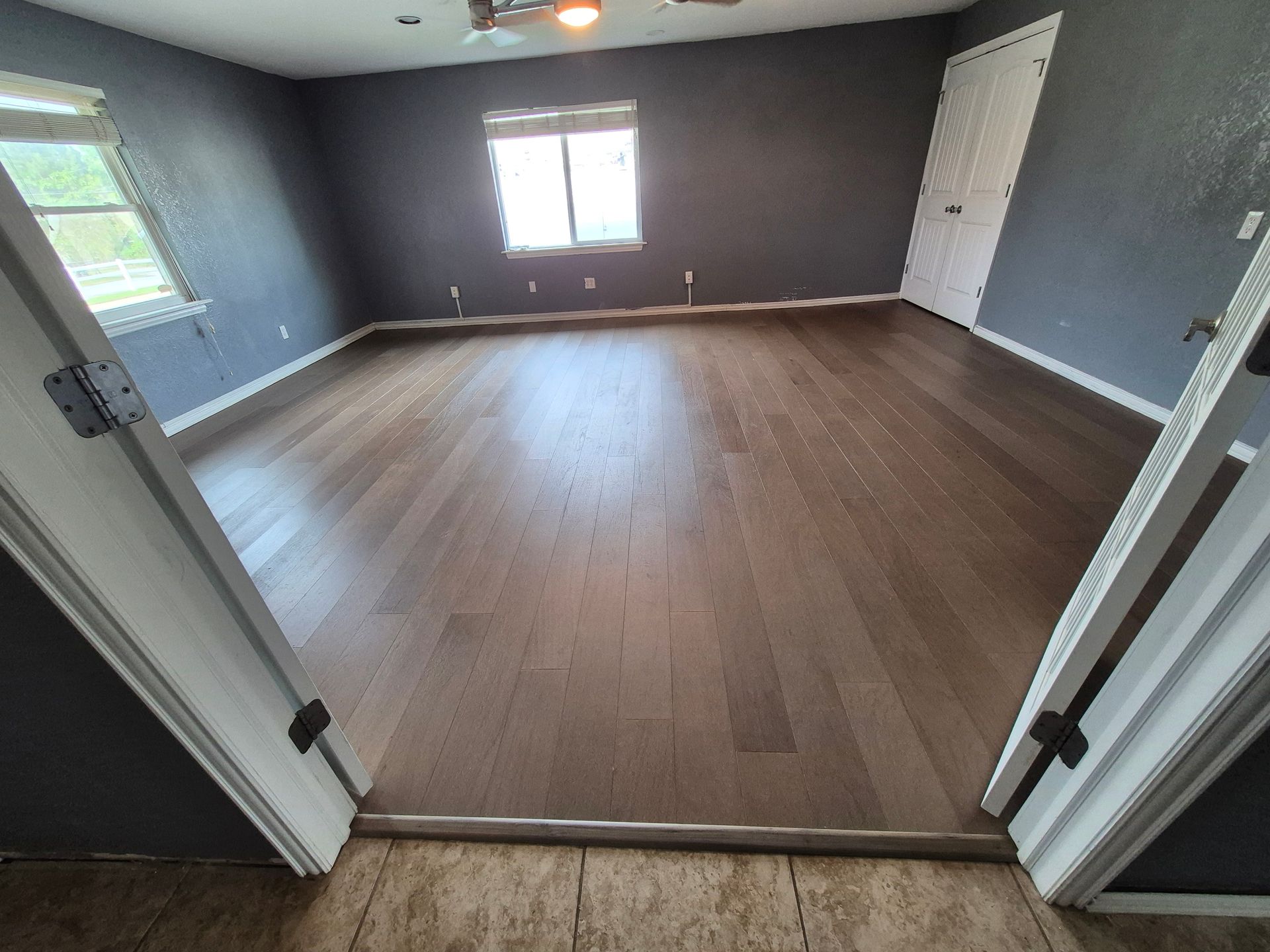 Dark wood floors in a mostly empty room with gray walls, two open doorways, and a window.