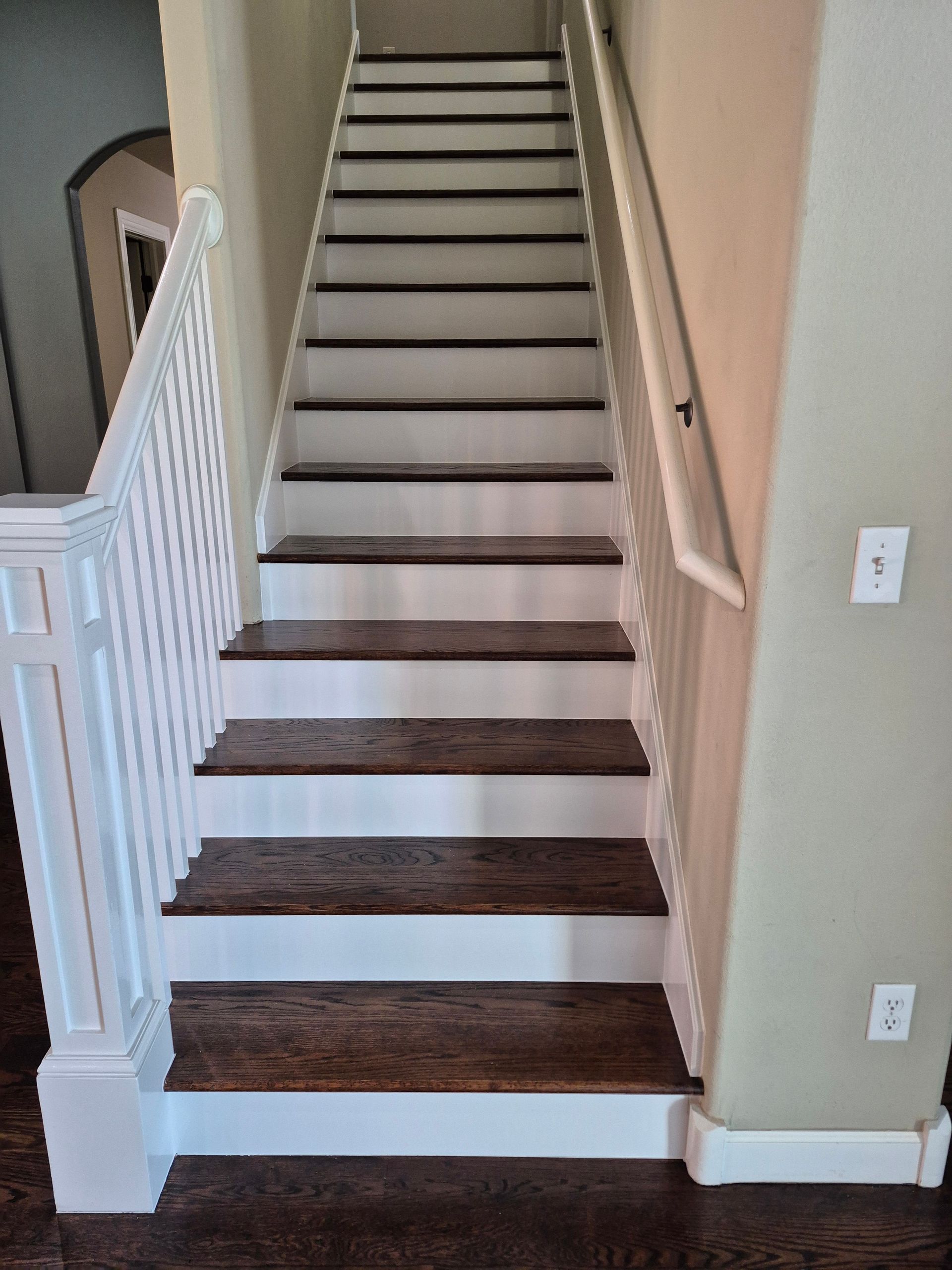 Wooden staircase with dark brown treads and white risers and railing, against tan walls.