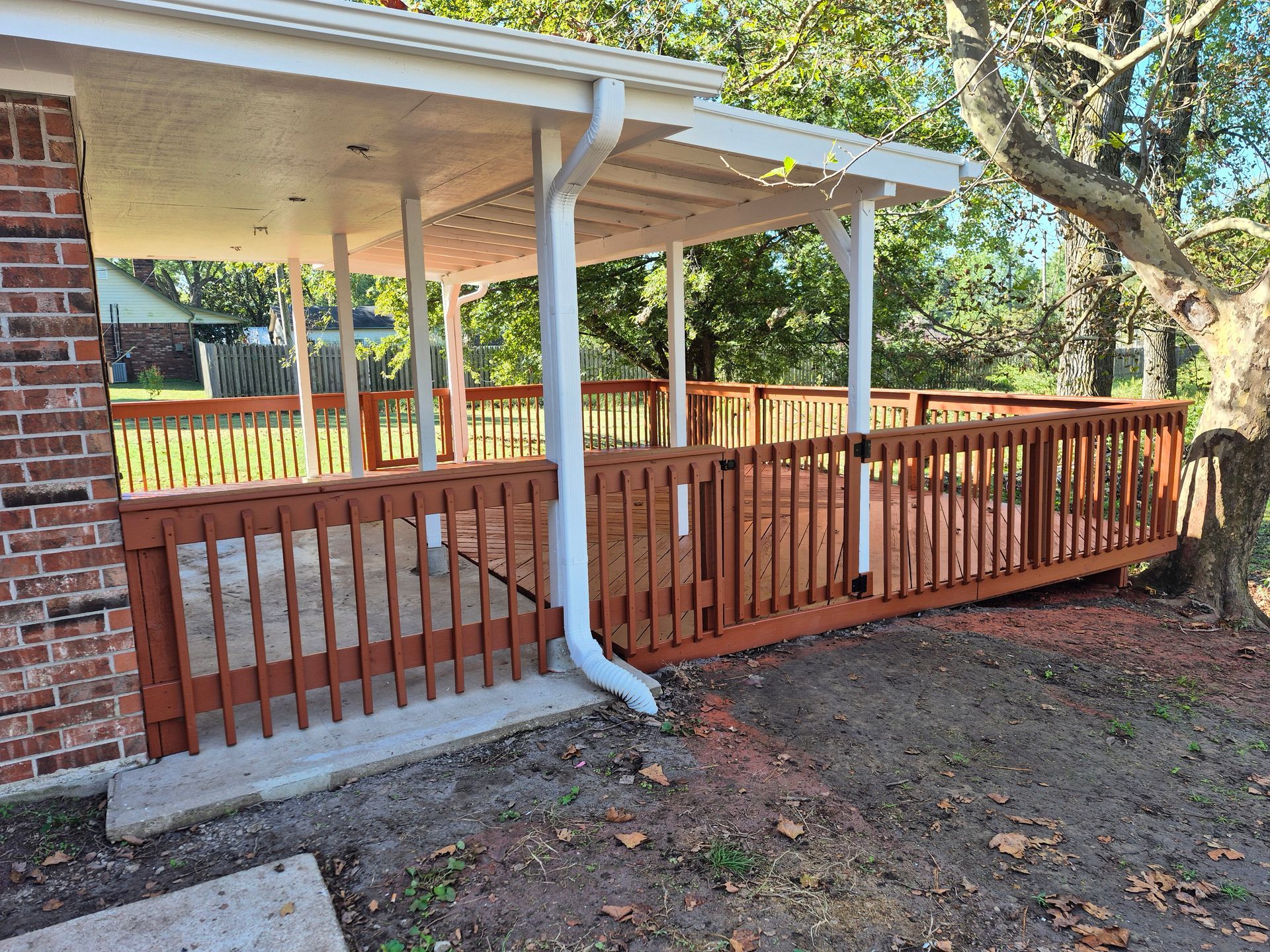 A wooden deck with a covered patio, next to a brick wall and a tree.