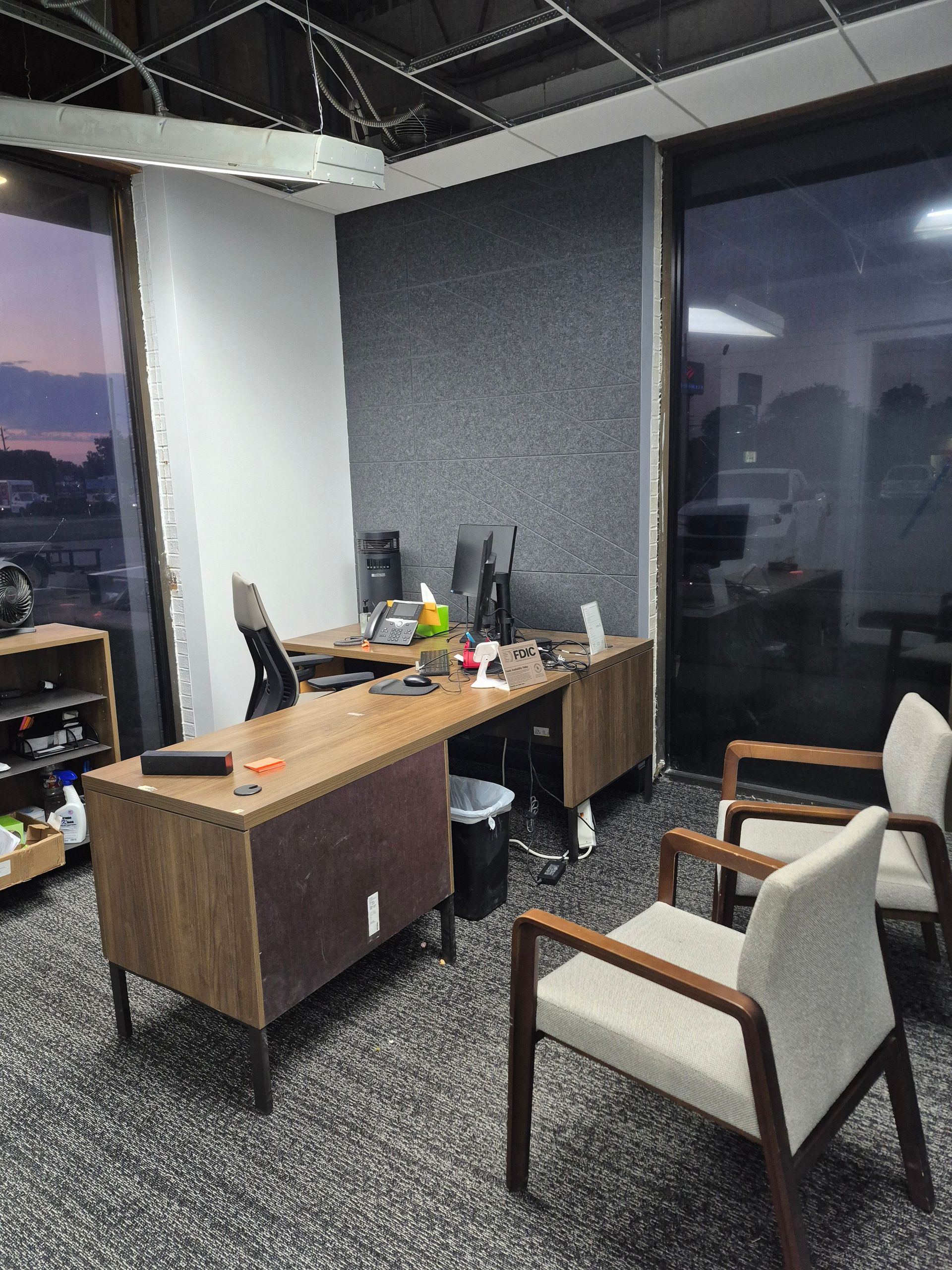 Office desk with two chairs, gray textured wall, and large windows with city view.