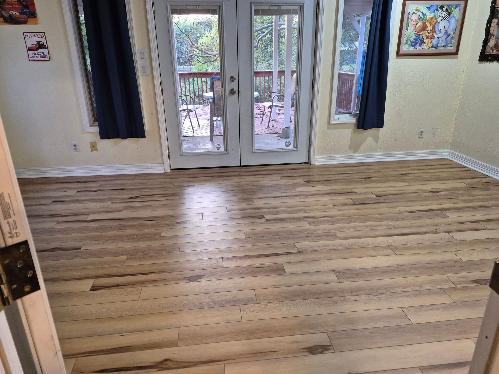 Room with light wood-look flooring, glass doors to a deck, windows with blue curtains, and artwork on the wall.