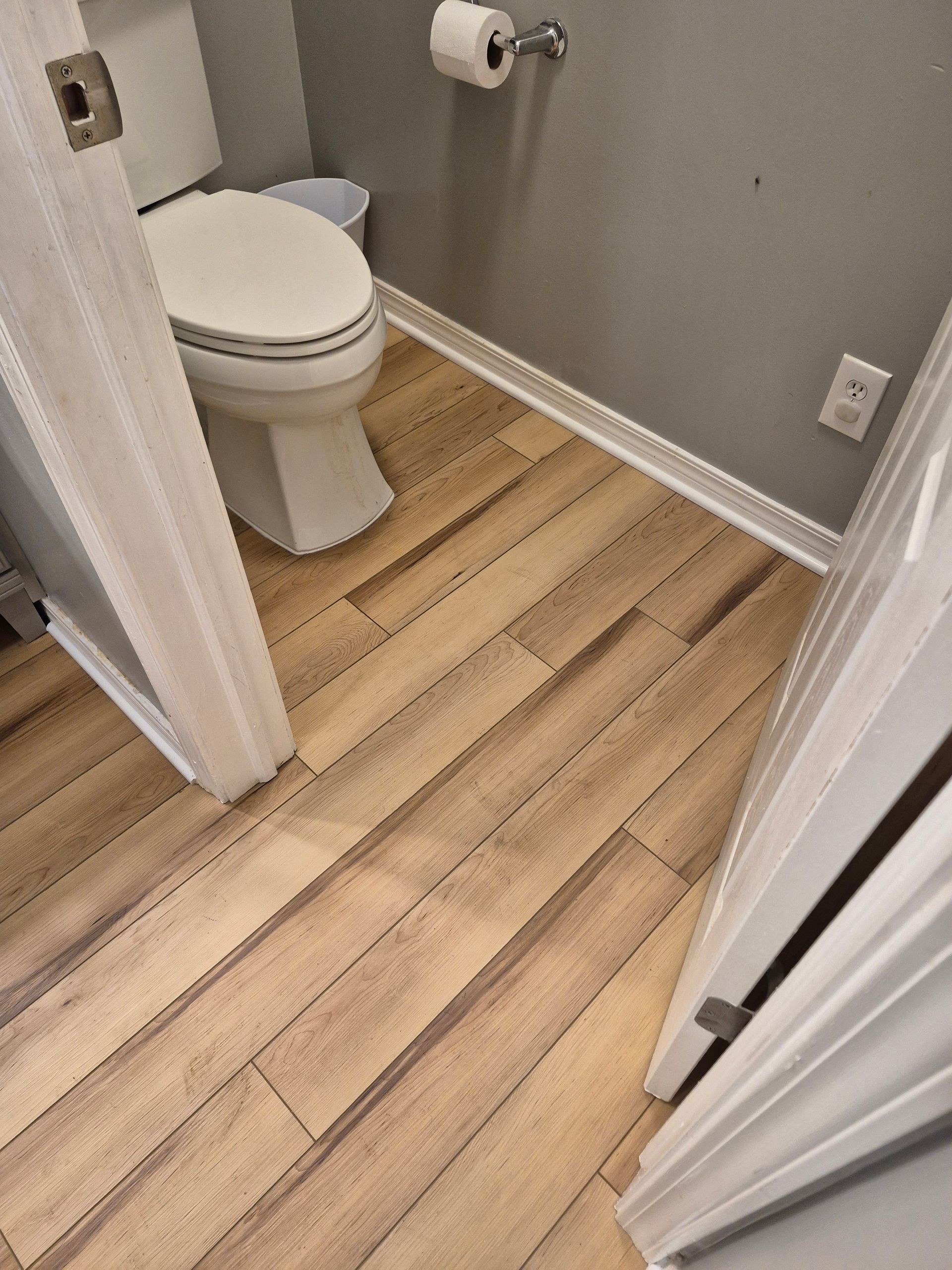 Bathroom with light wood-look floor tiles, white toilet, gray walls, and white trim.