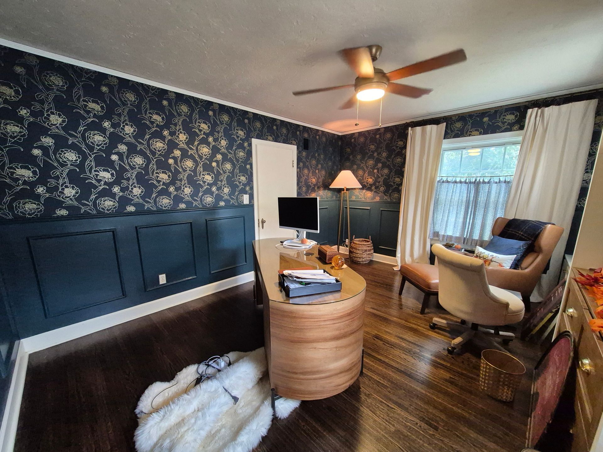 Home office with dark blue floral wallpaper, wood paneling, desk, and chair.