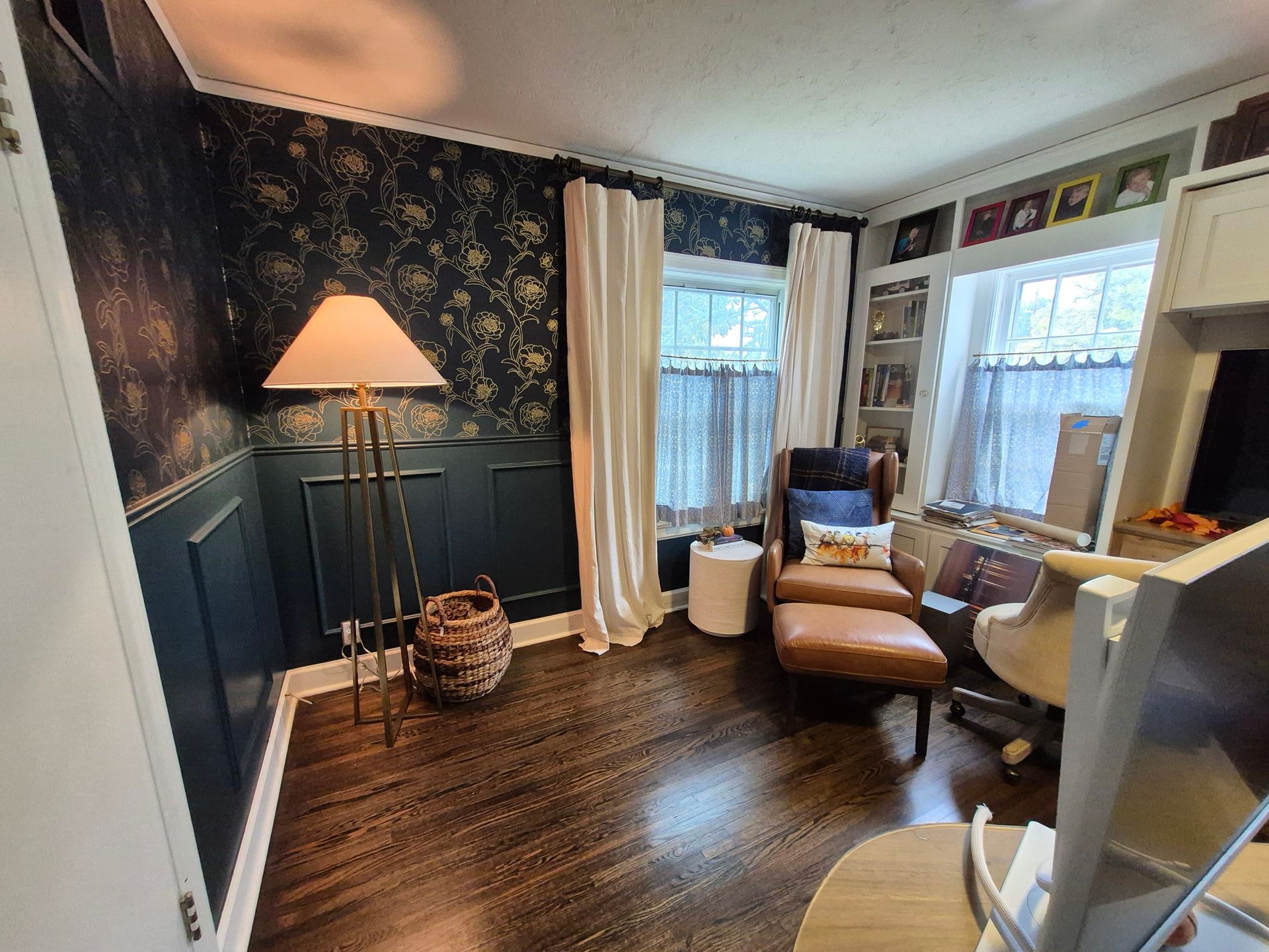 Cozy home office with dark floral wallpaper, wood trim, curtains, a leather chair with ottoman, and a desk.