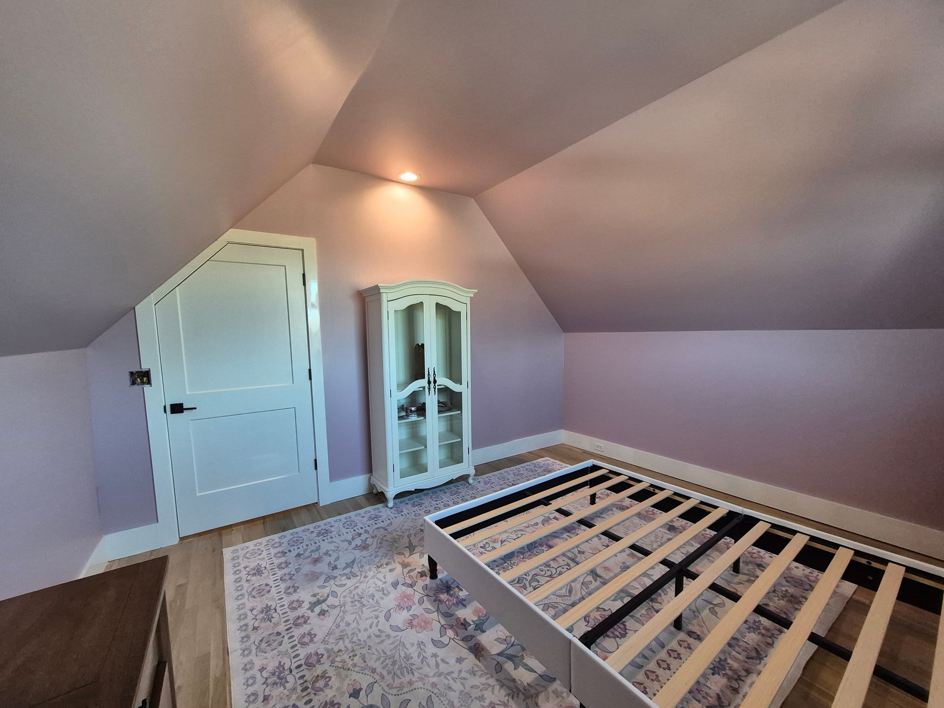 Bedroom with angled ceiling, light purple walls, and wooden bed frame on a patterned rug.