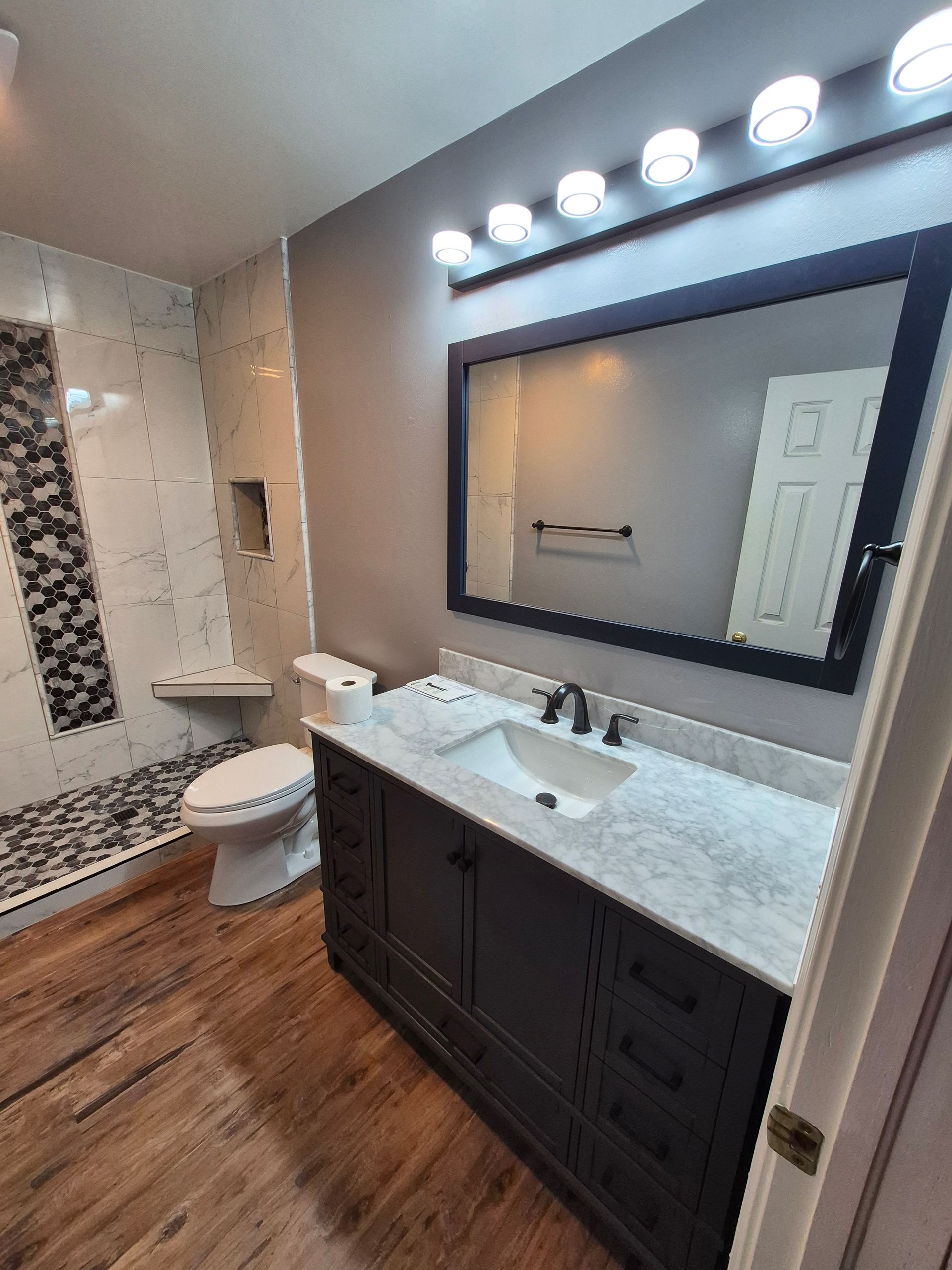 Bathroom with dark vanity, large mirror, and shower with patterned tile. Wooden floor.