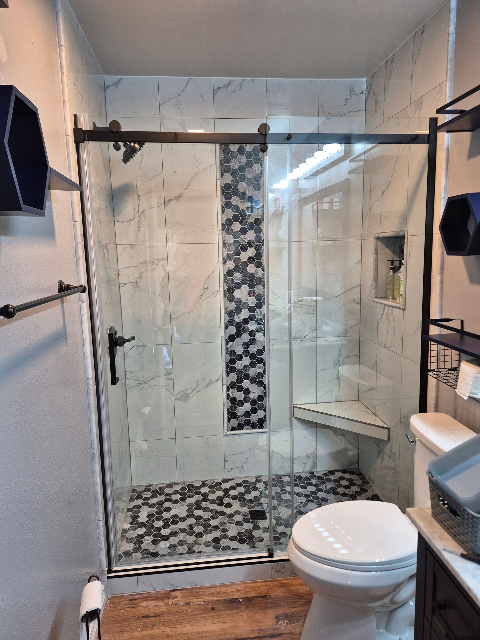Bathroom with glass shower, patterned tile, dark hardware, and a toilet.