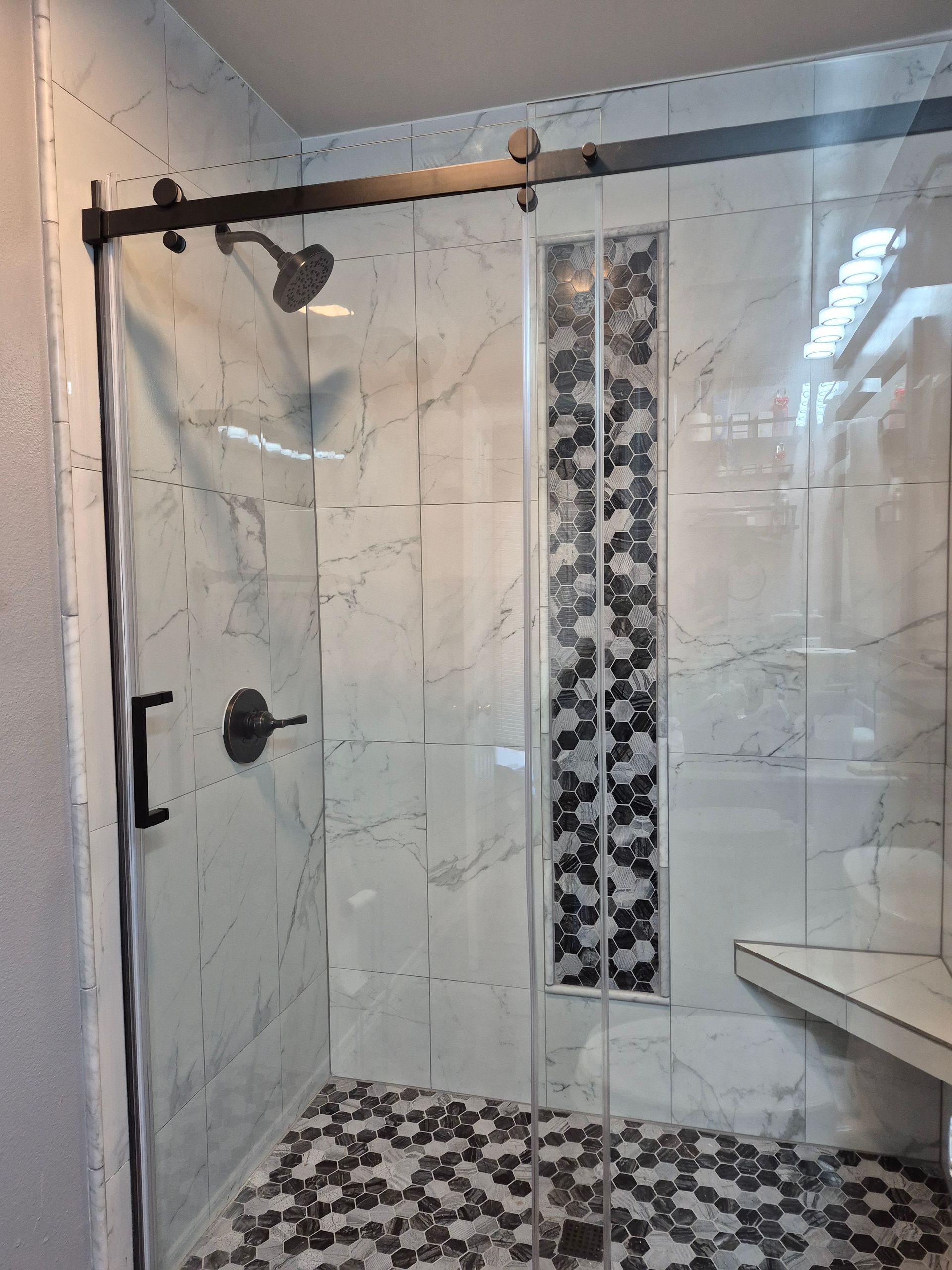 Glass shower enclosure with black hardware, marble tile walls, and mosaic tile floor.