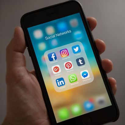 A person is holding a cell phone with social networks on the screen