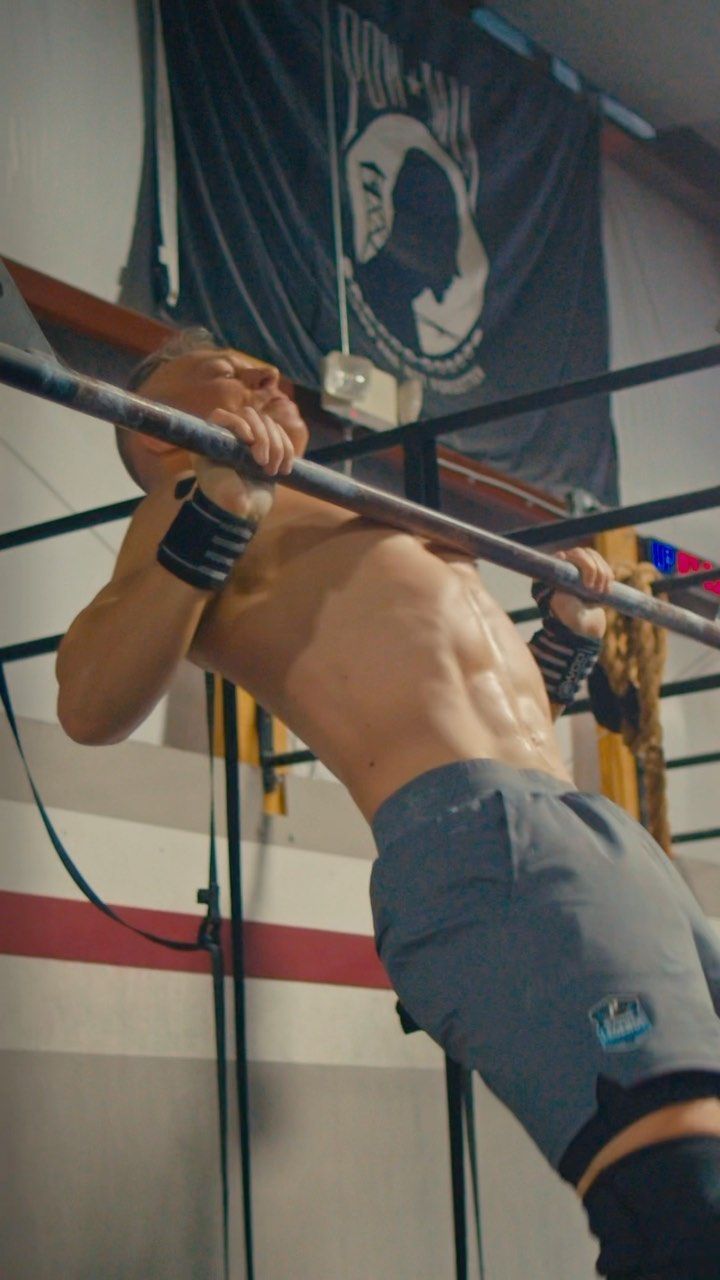 A shirtless man is doing a pull up on a bar in a gym.