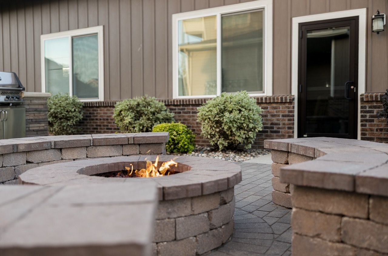Outdoor community courtyard with a circular brick fire pit and seating near an apartment entrance.