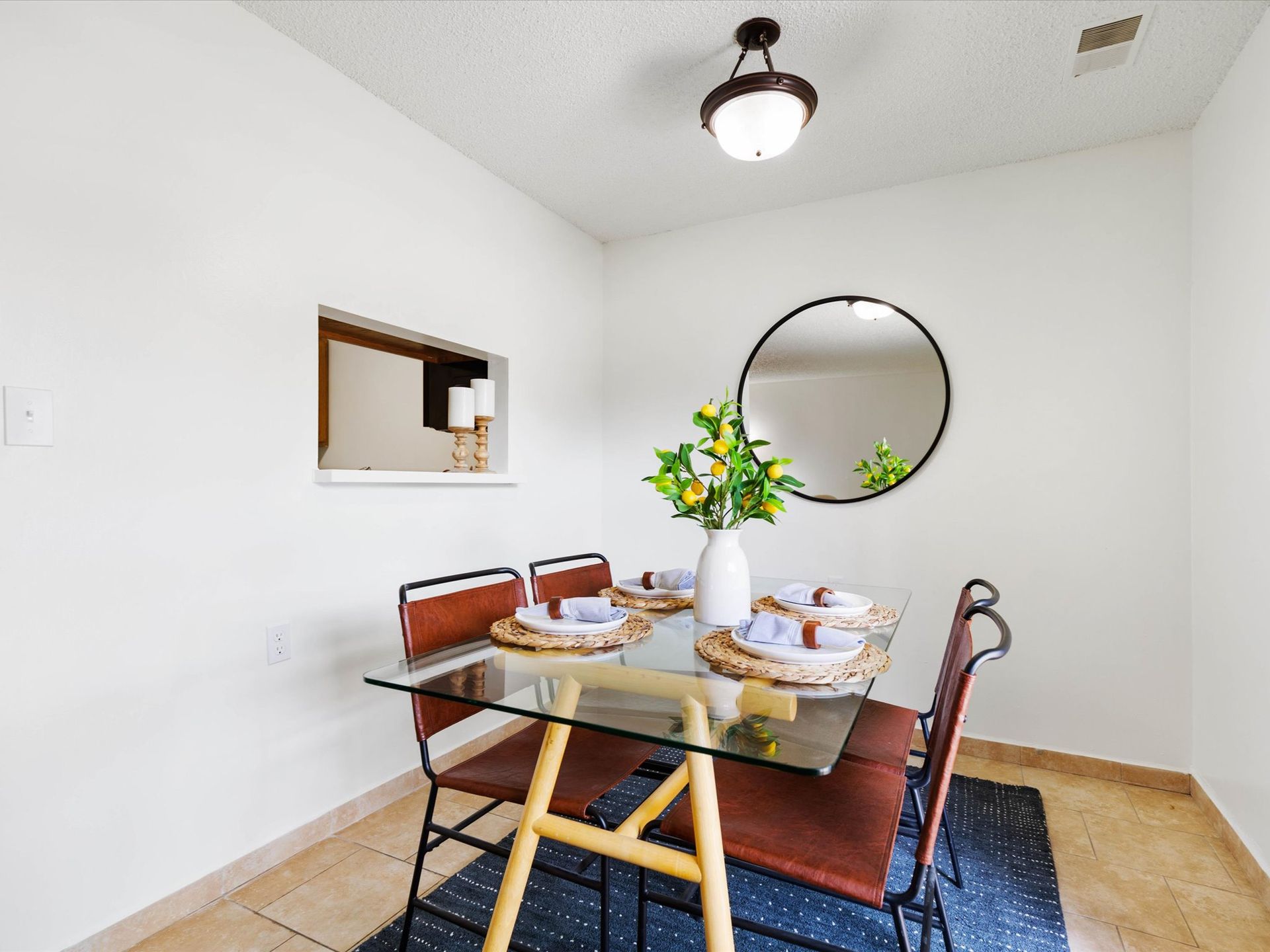 Dining room with glass table, four chairs, mirror, and floral arrangement on the table.
