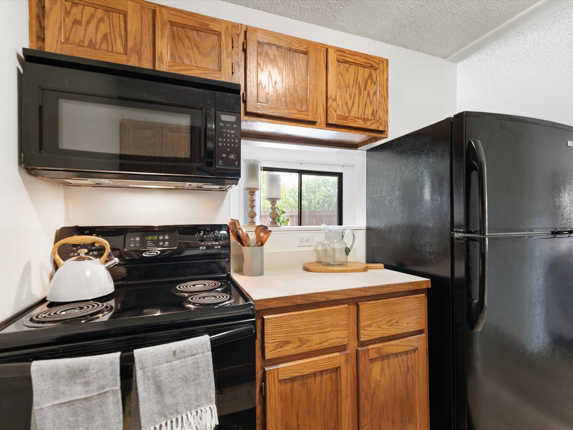 Small kitchen with black appliances, wooden cabinets, and white countertop.