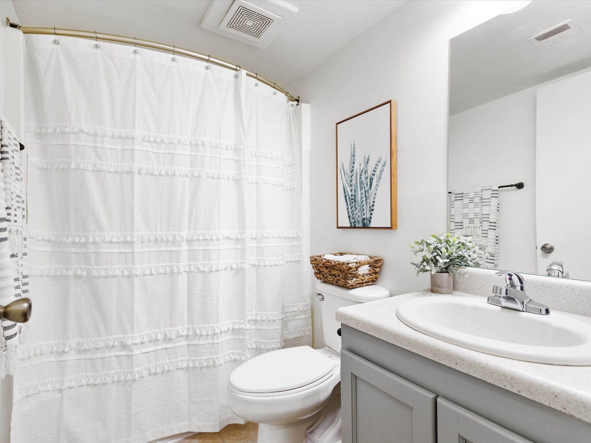 Bathroom with white shower curtain, toilet, sink, artwork, and gray cabinets.
